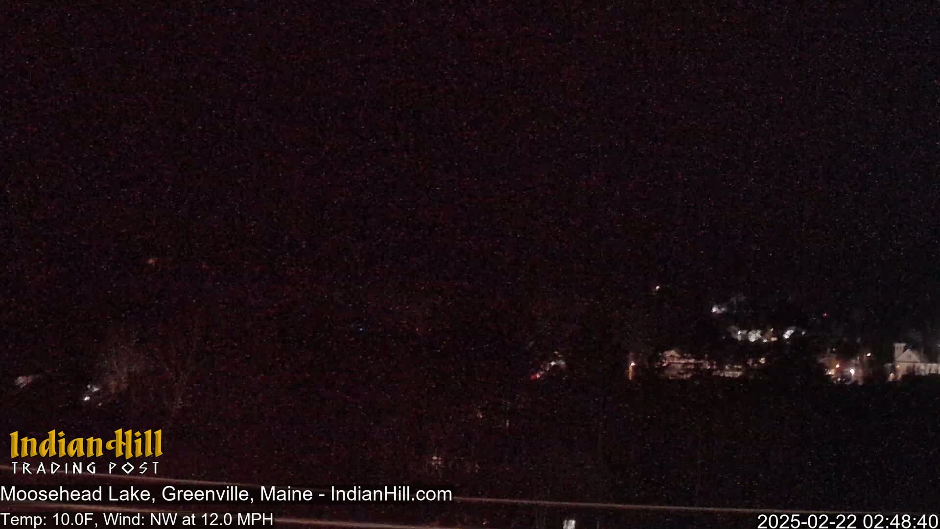 A nighttime long shot shows a dimly lit town in the distance under a dark, clear sky, with a northwest wind blowing at 12 mph and a temperature of 10 degrees Fahrenheit.