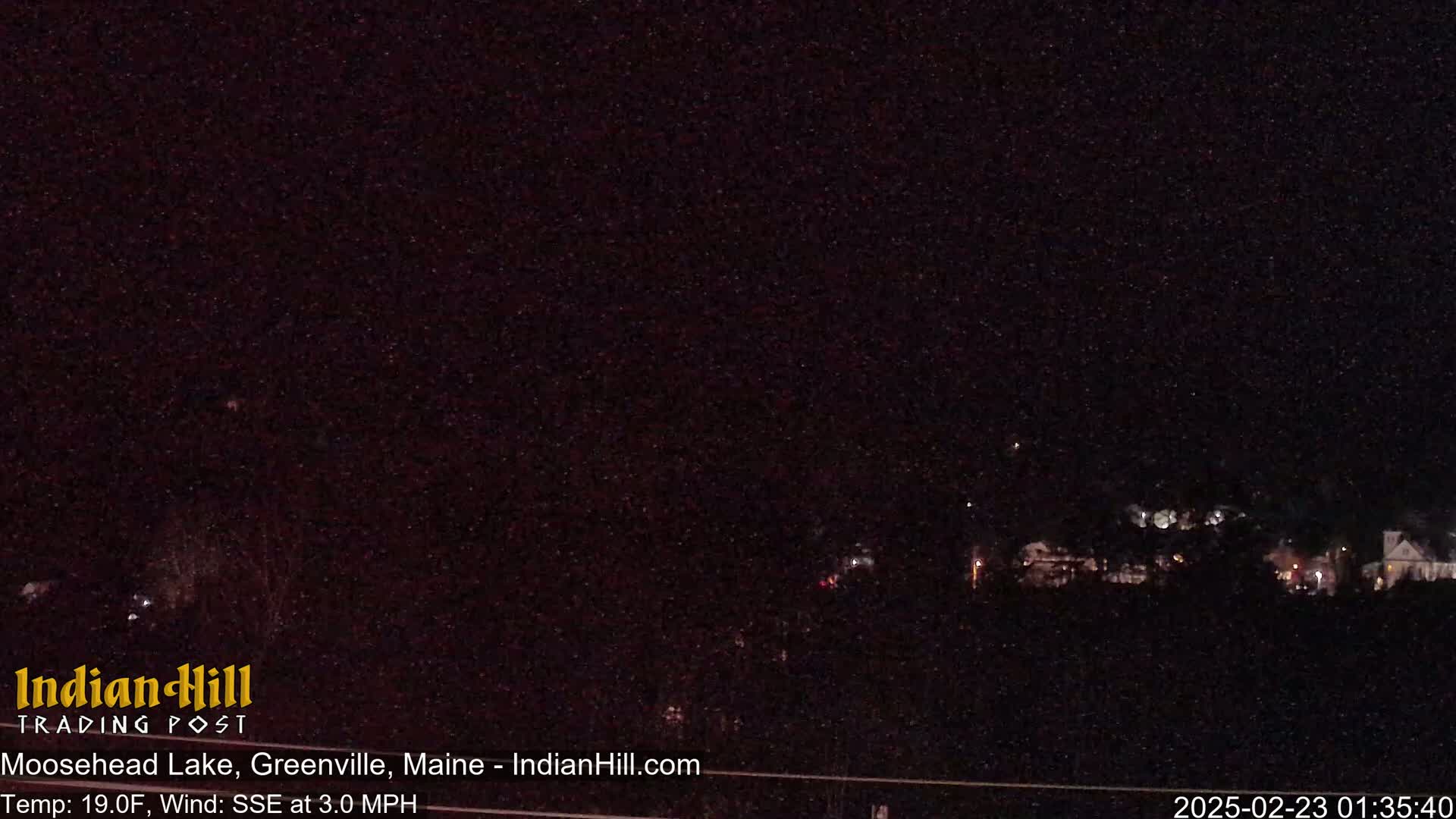 A nighttime long shot of dimly lit houses and trees under a dark, clear sky.