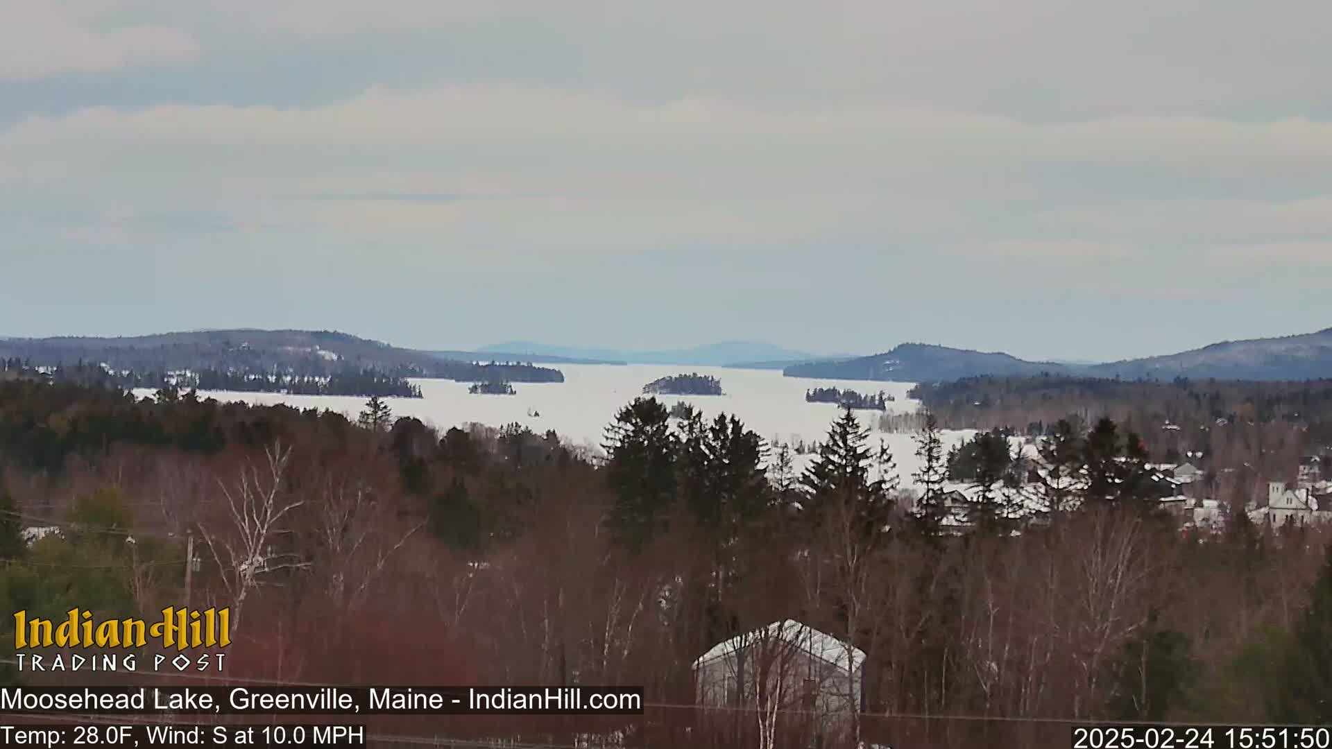 A snow-covered lake stretches between wooded hills under a cloudy sky.