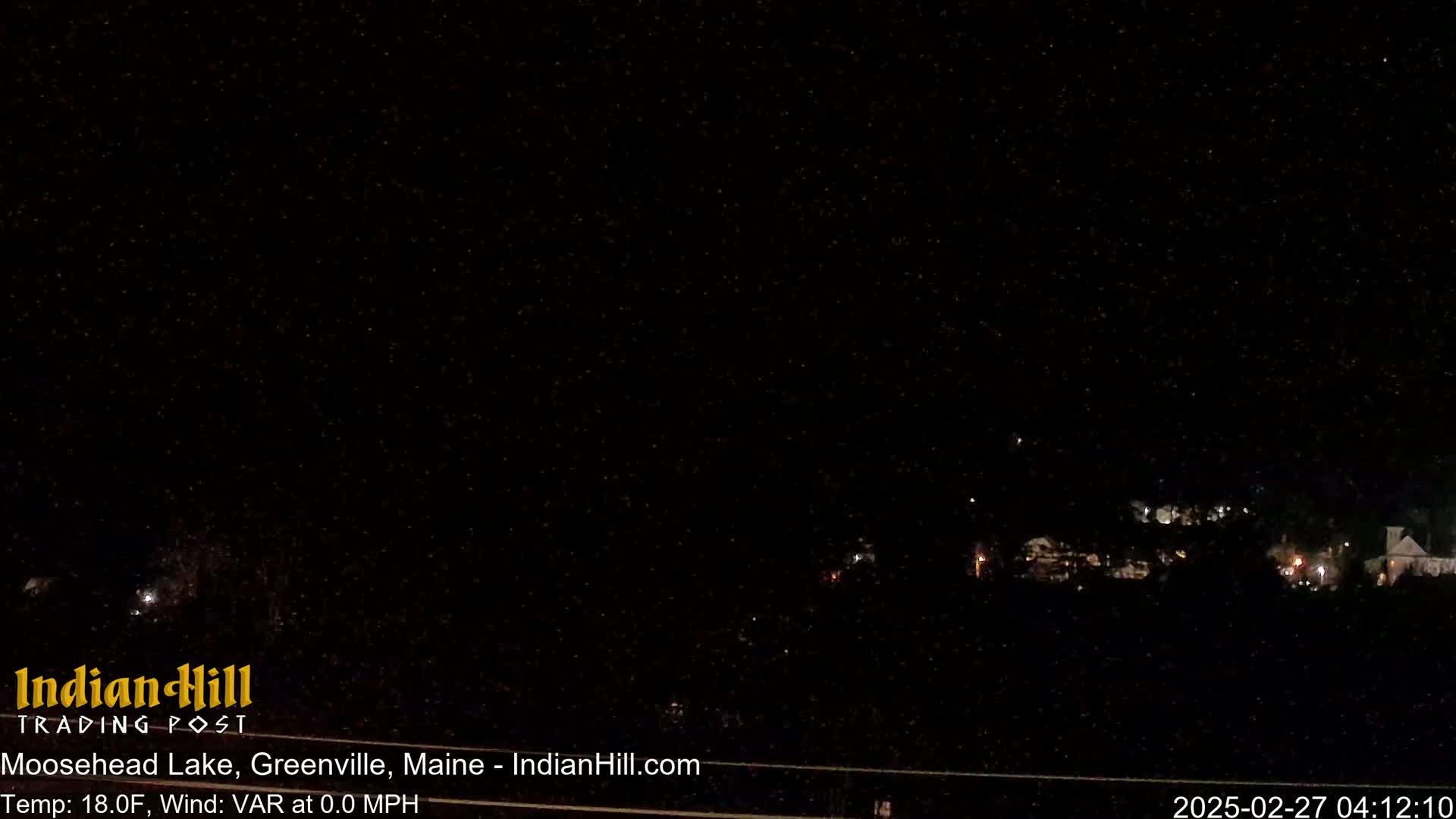 A nighttime, dark outdoor scene shows a few faint lights in the distance under a starry sky.