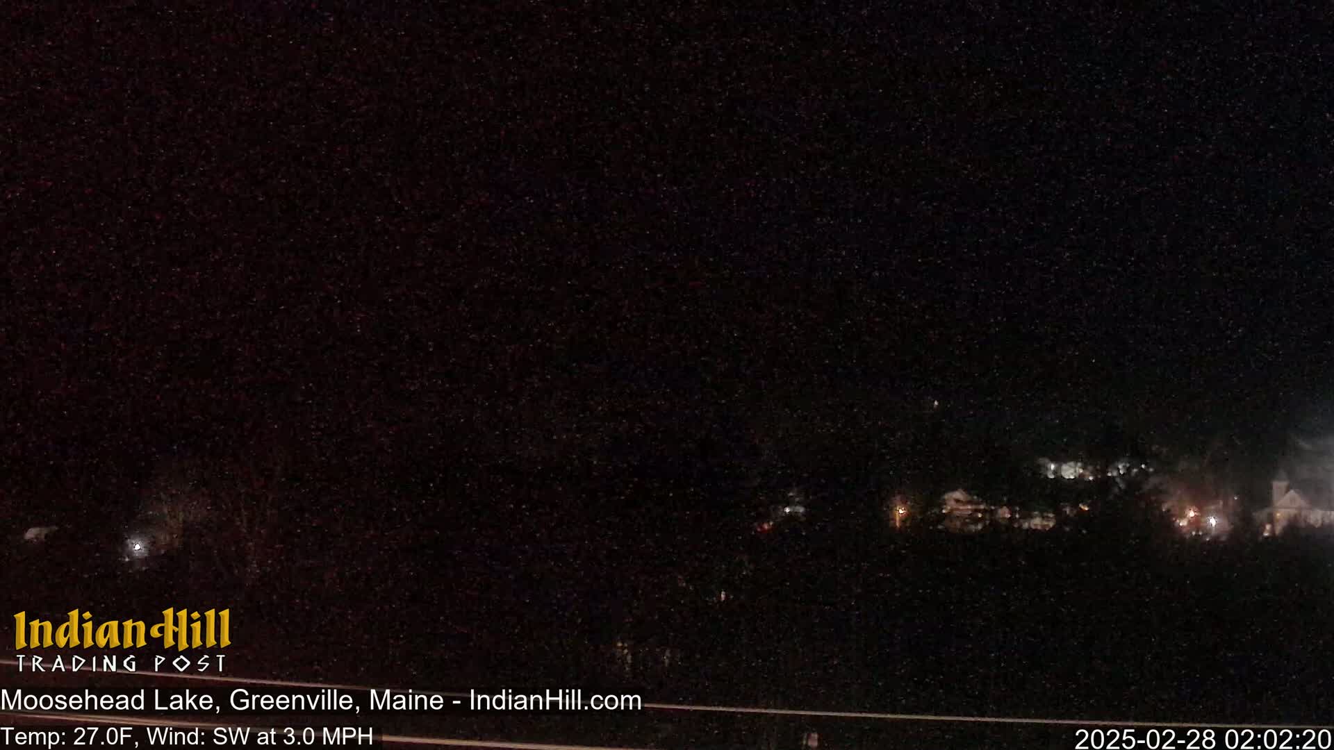 A nighttime, dark view of a landscape with a few distant lights under a mostly clear sky, with a light southwest wind at 3 mph and a temperature of 27 degrees Fahrenheit.