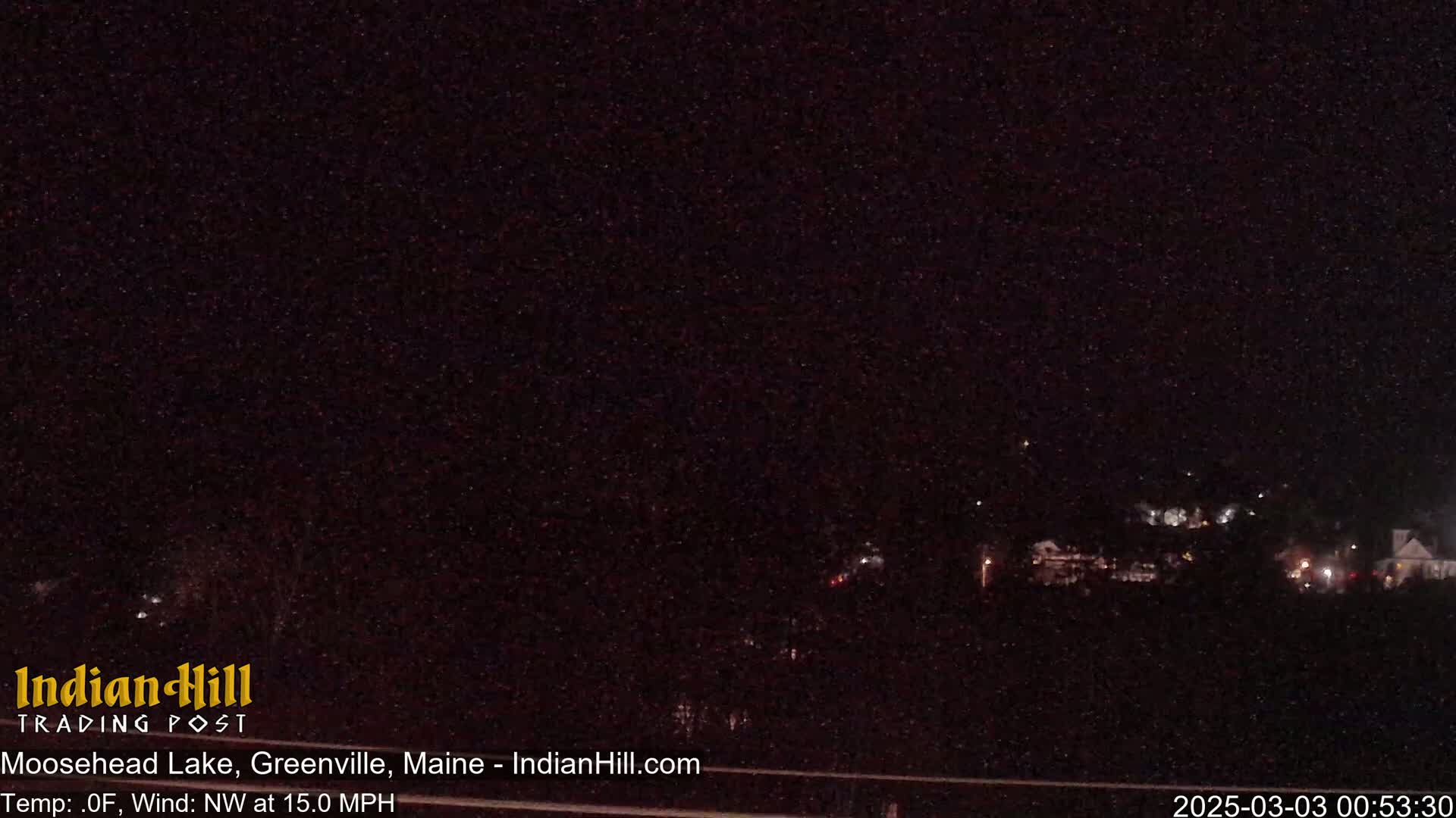 A nighttime, long shot of a dark landscape with a few distant lights under a clear, dark sky with a northwest wind at 15 mph.