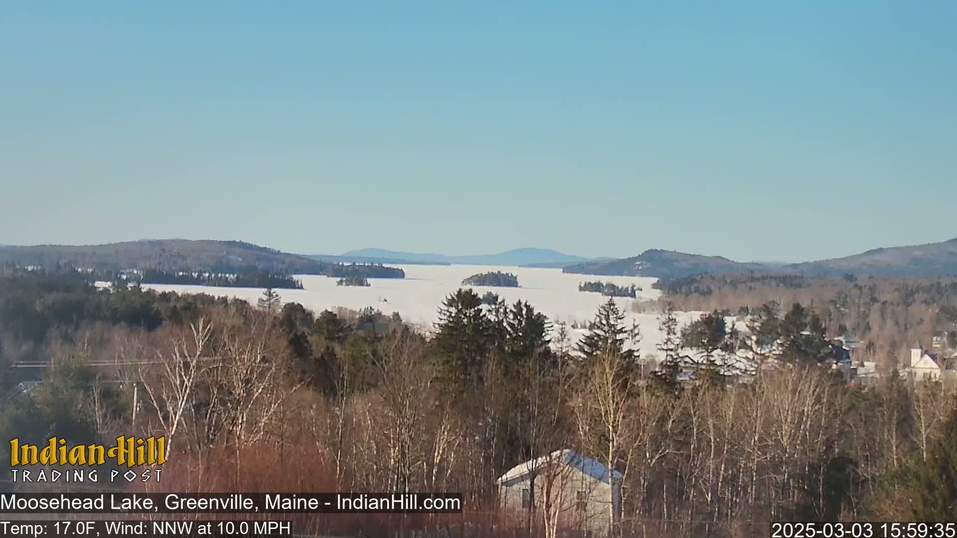 A frozen lake stretches to distant snow-covered hills under a clear blue sky.