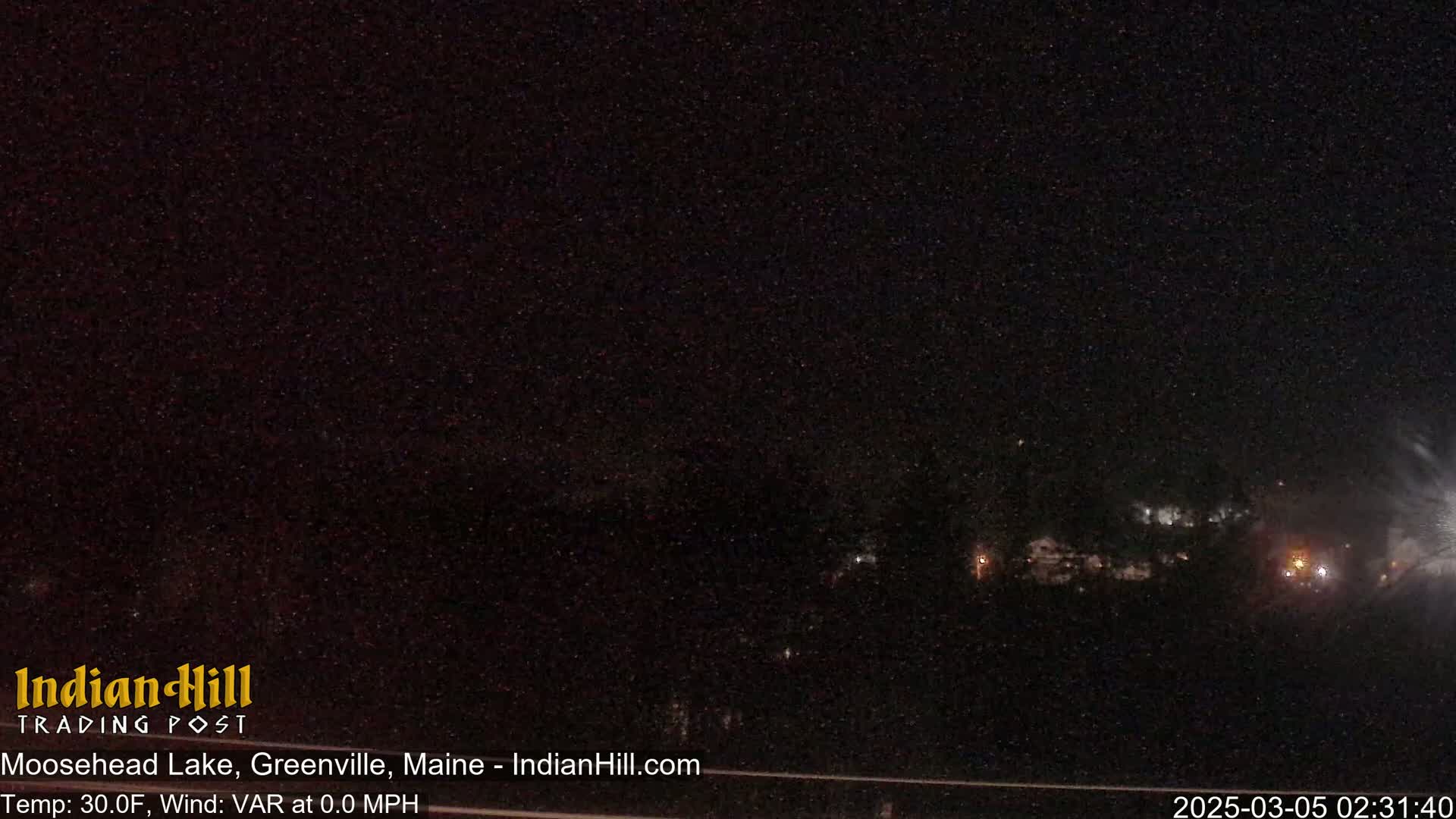 A nighttime, dark outdoor scene shows a mostly obscured horizon line with faint lights visible in the distance under a clear, starry sky.