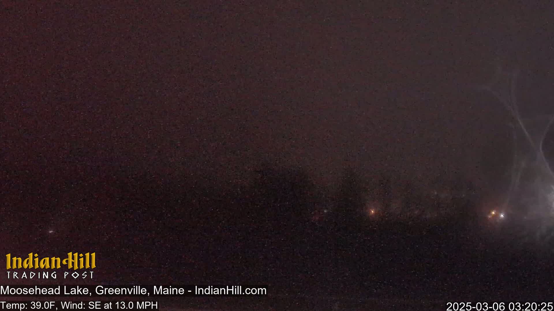 A dark, nighttime scene with a few faint lights in the distance under a hazy, possibly snowy sky, with a southeast wind.