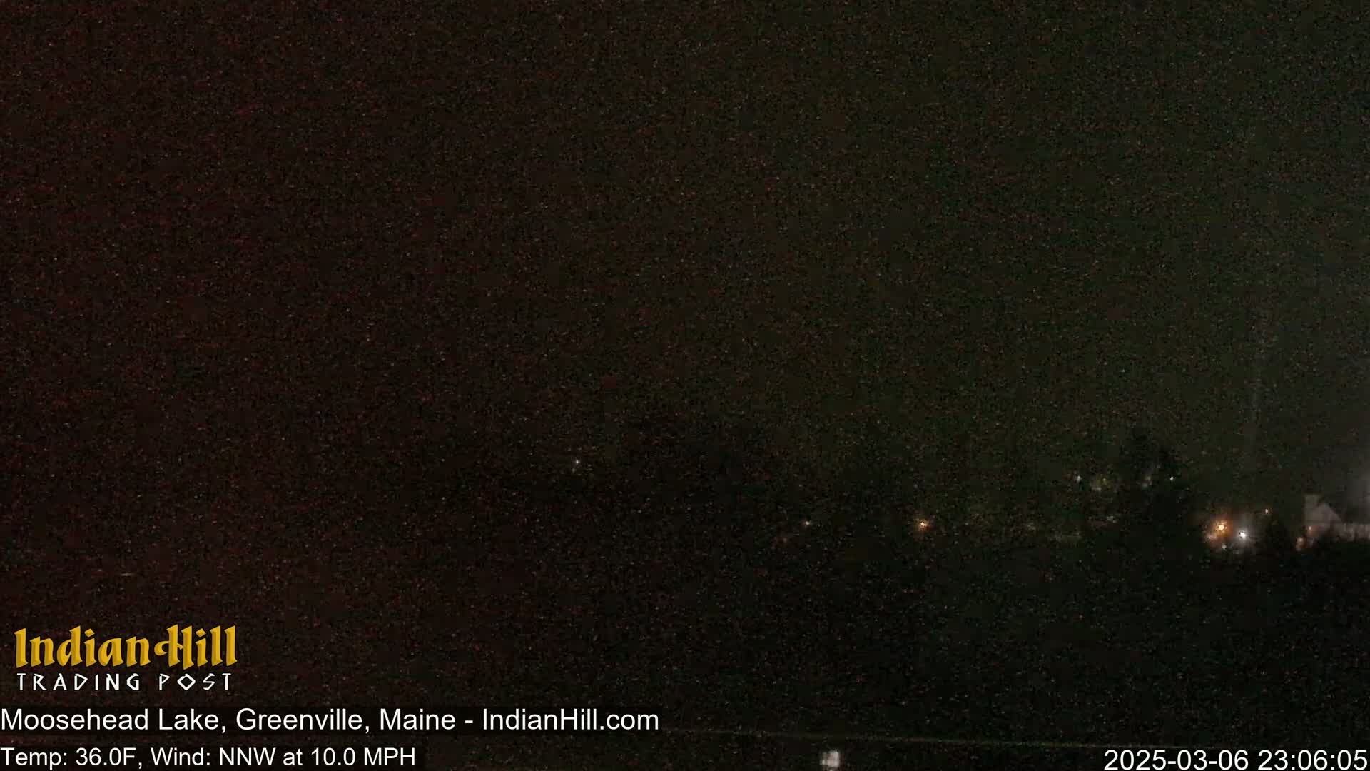 A nighttime long shot of a dark landscape with a few distant lights under a dark sky.