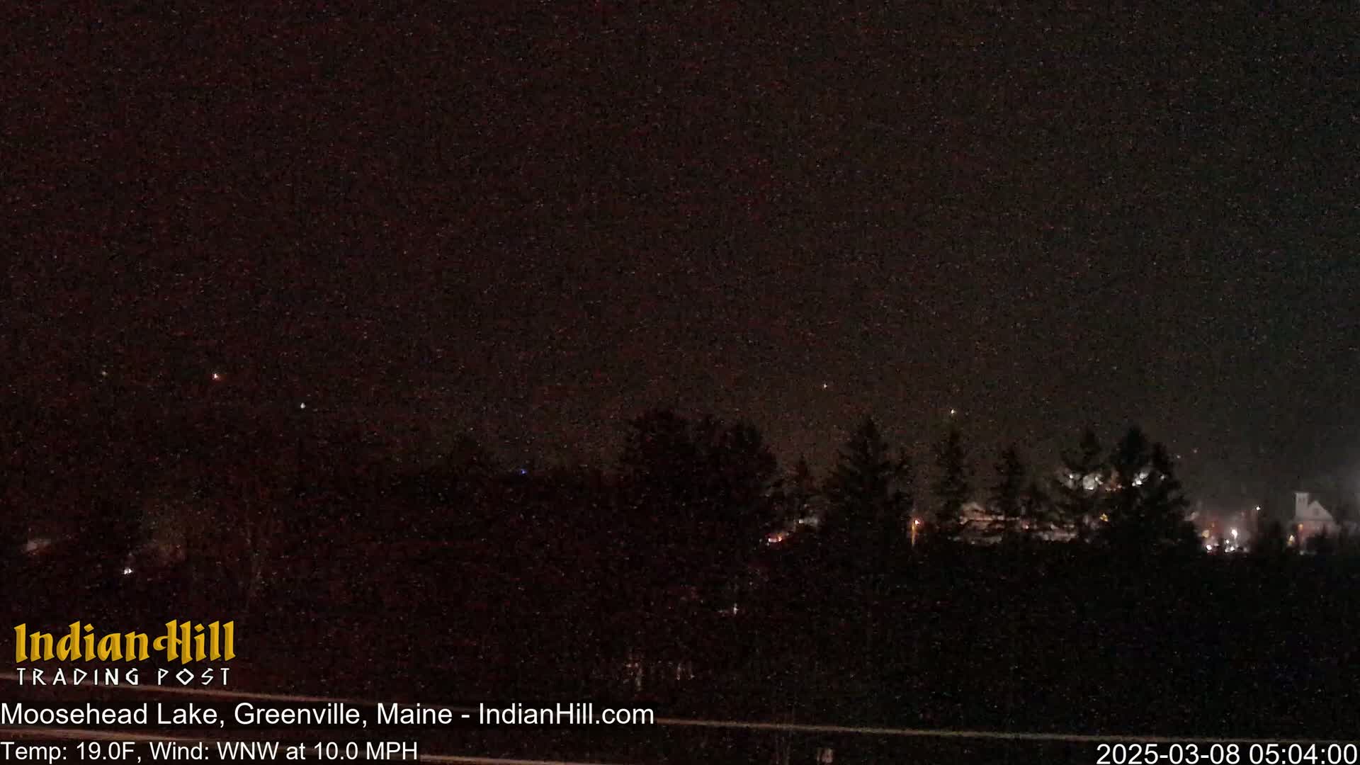 A nighttime view of a dark landscape with a few distant lights and a starry sky under windy, cold conditions.