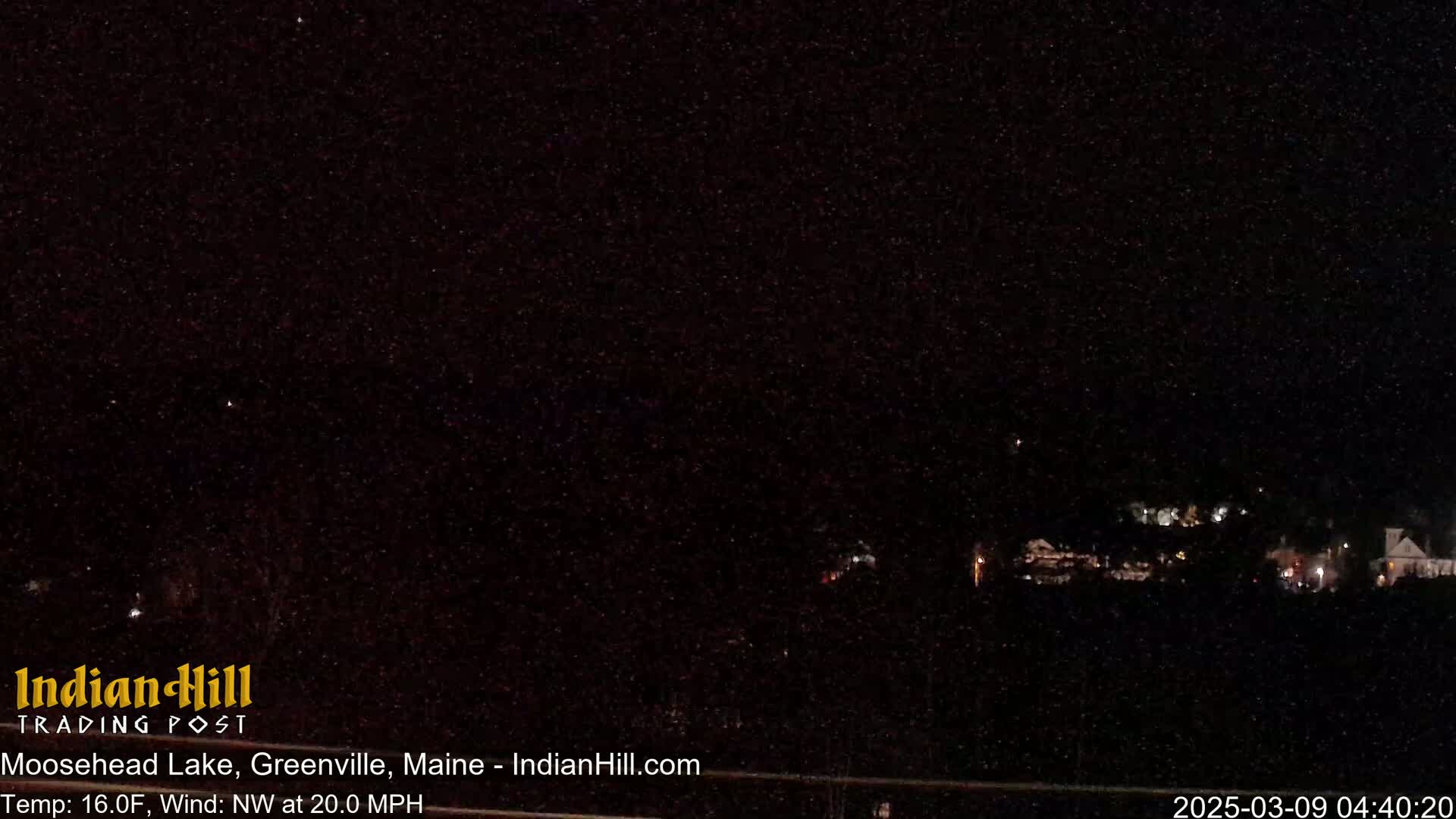 A nighttime long shot shows a distant cluster of lights against a dark, star-filled sky under a 16°F temperature with a 20 mph northwest wind.