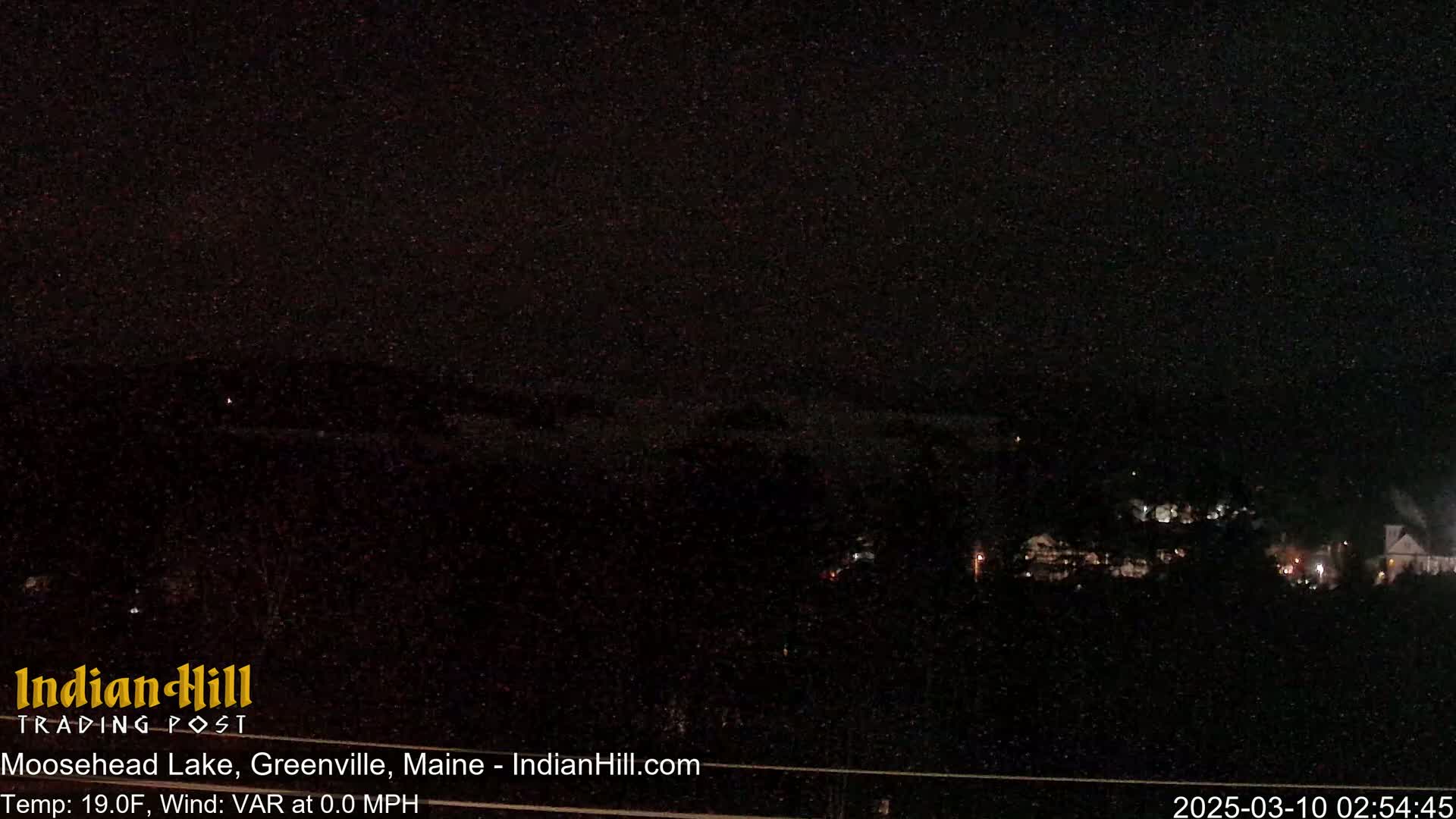 A nighttime view of a dark lake and distant lights under snowy conditions.