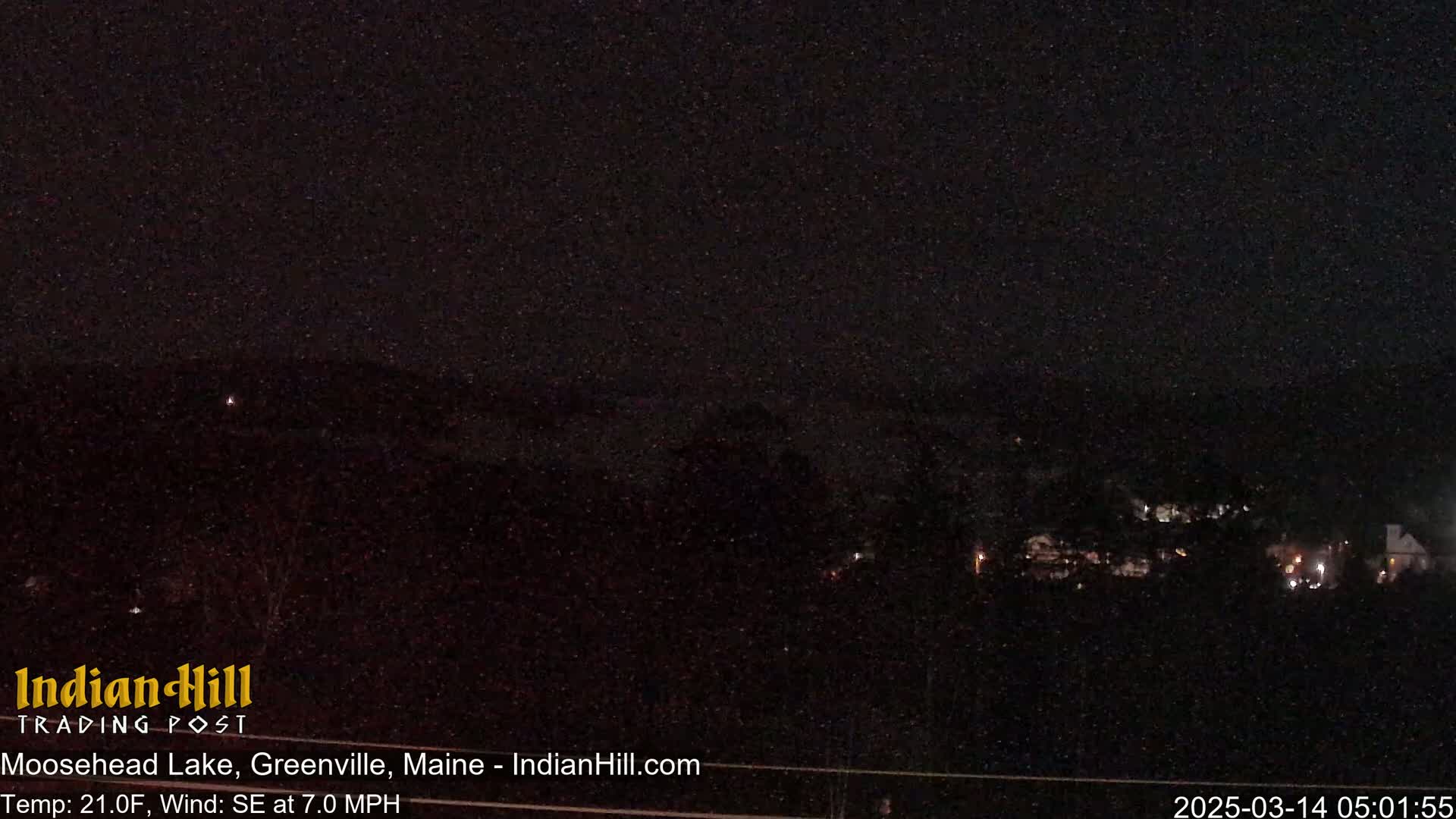 A nighttime view of a dark lake and distant lights under a dark, possibly snowy sky with a southeast wind.