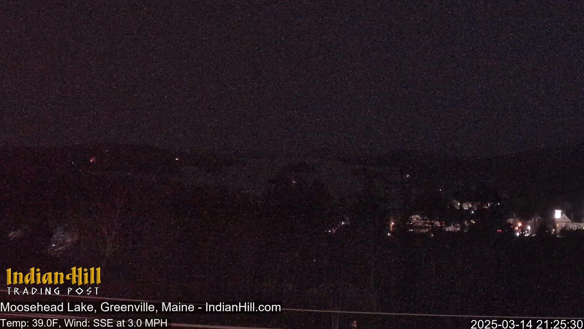 A nighttime long shot of a lake and distant buildings under a dark, snowy sky.