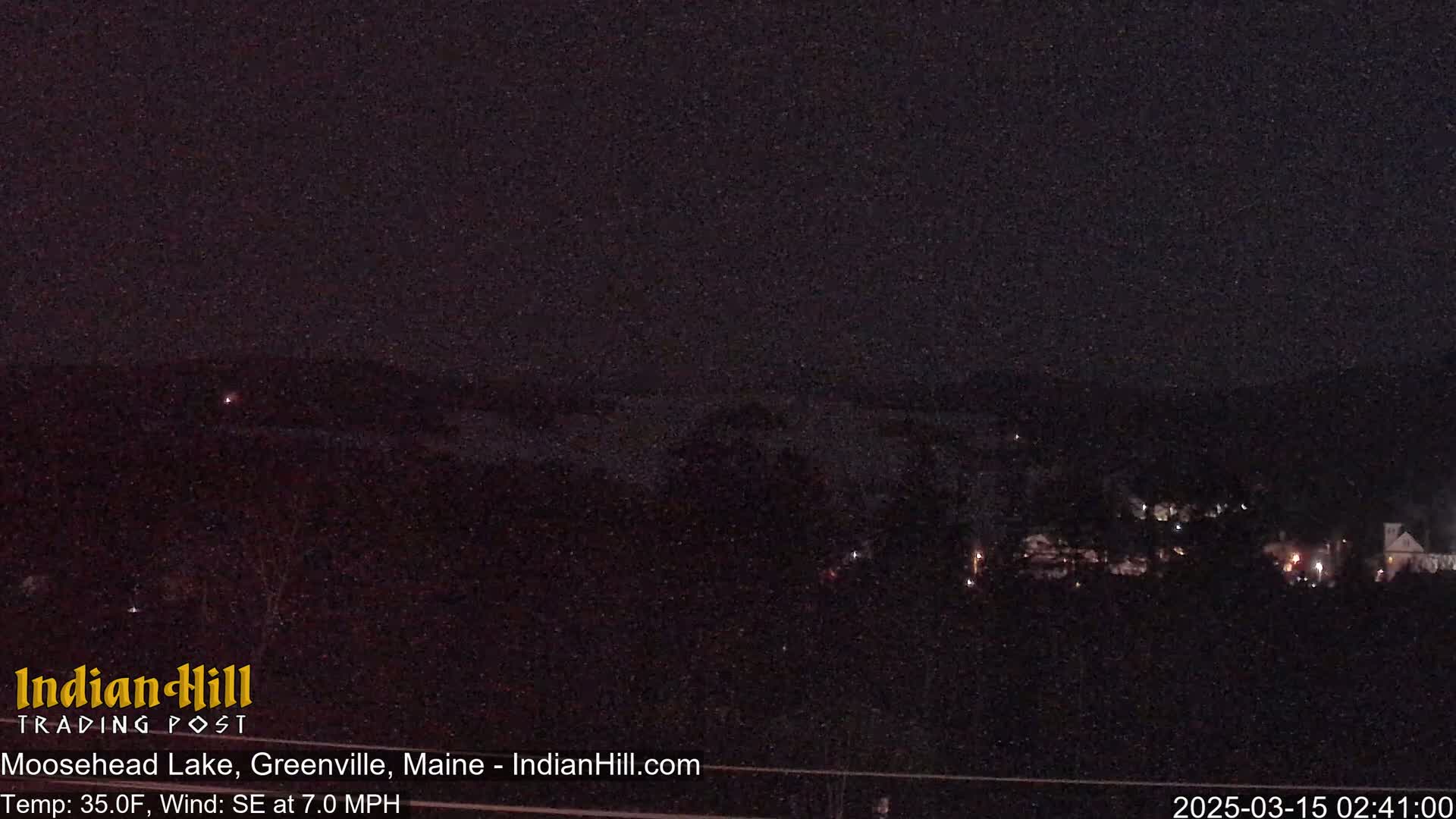 A nighttime view of a lake and distant buildings under a dark, possibly snowy sky.