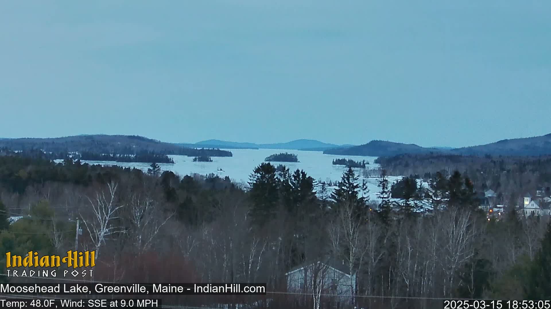 A partially frozen lake is visible from a snowy, wooded hillside under a twilight sky.
