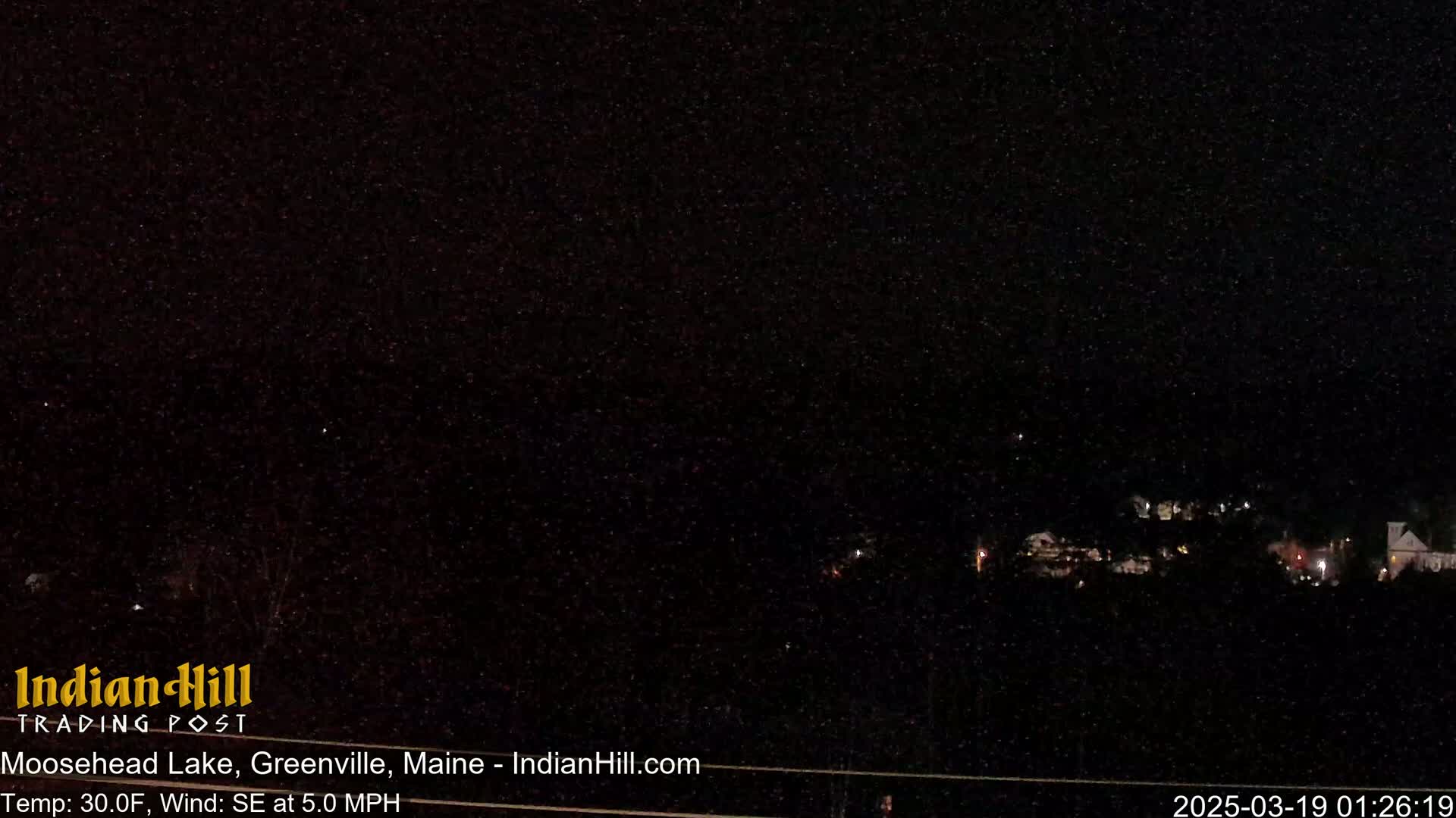 A nighttime view of a dark landscape with a few distant lights under a starry sky, with a light southeast wind and a temperature of 30 degrees Fahrenheit.