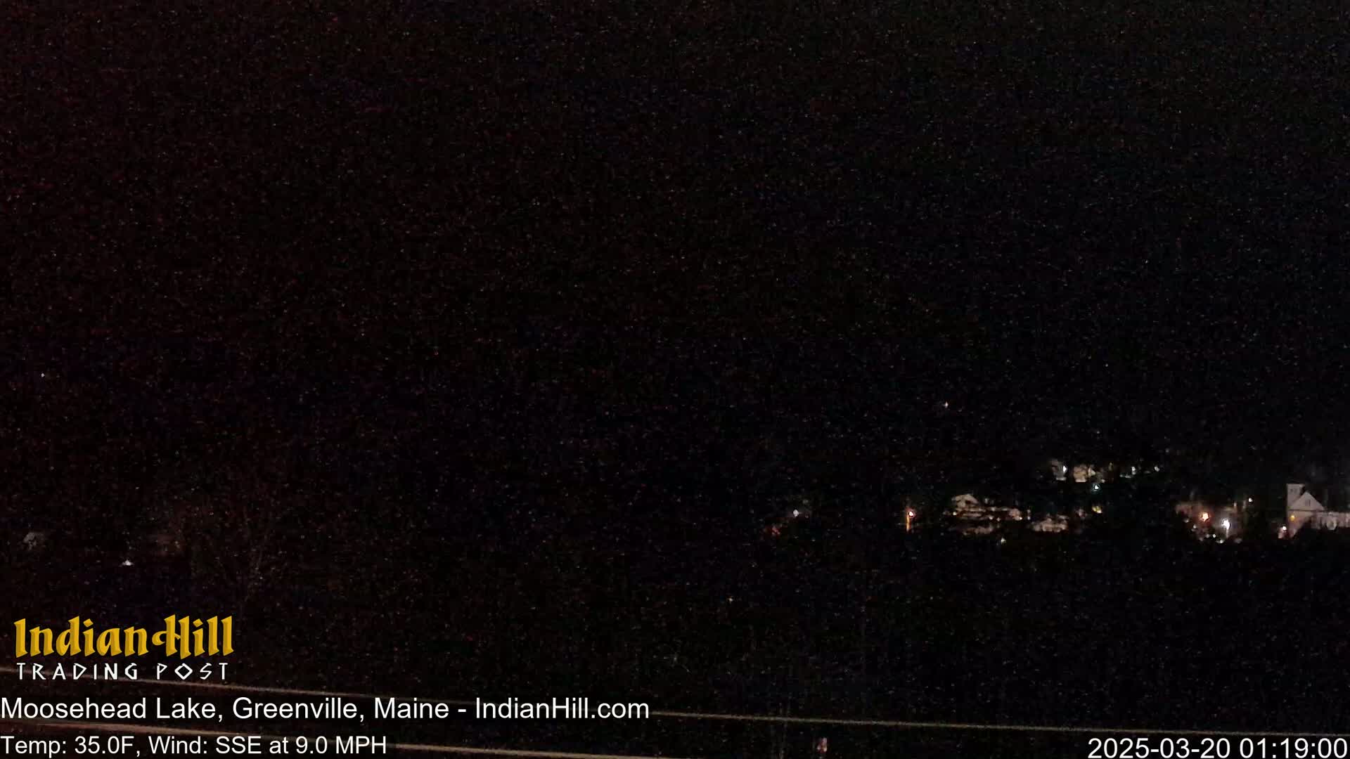 A nighttime, dark image shows a small town in the distance under a dark, possibly snowy sky.