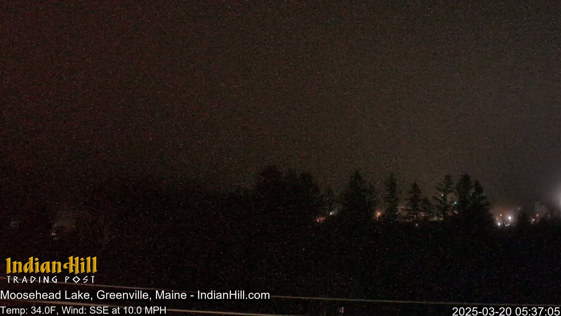 A nighttime view of a dark, tree-lined horizon under a hazy sky with a SSE wind.