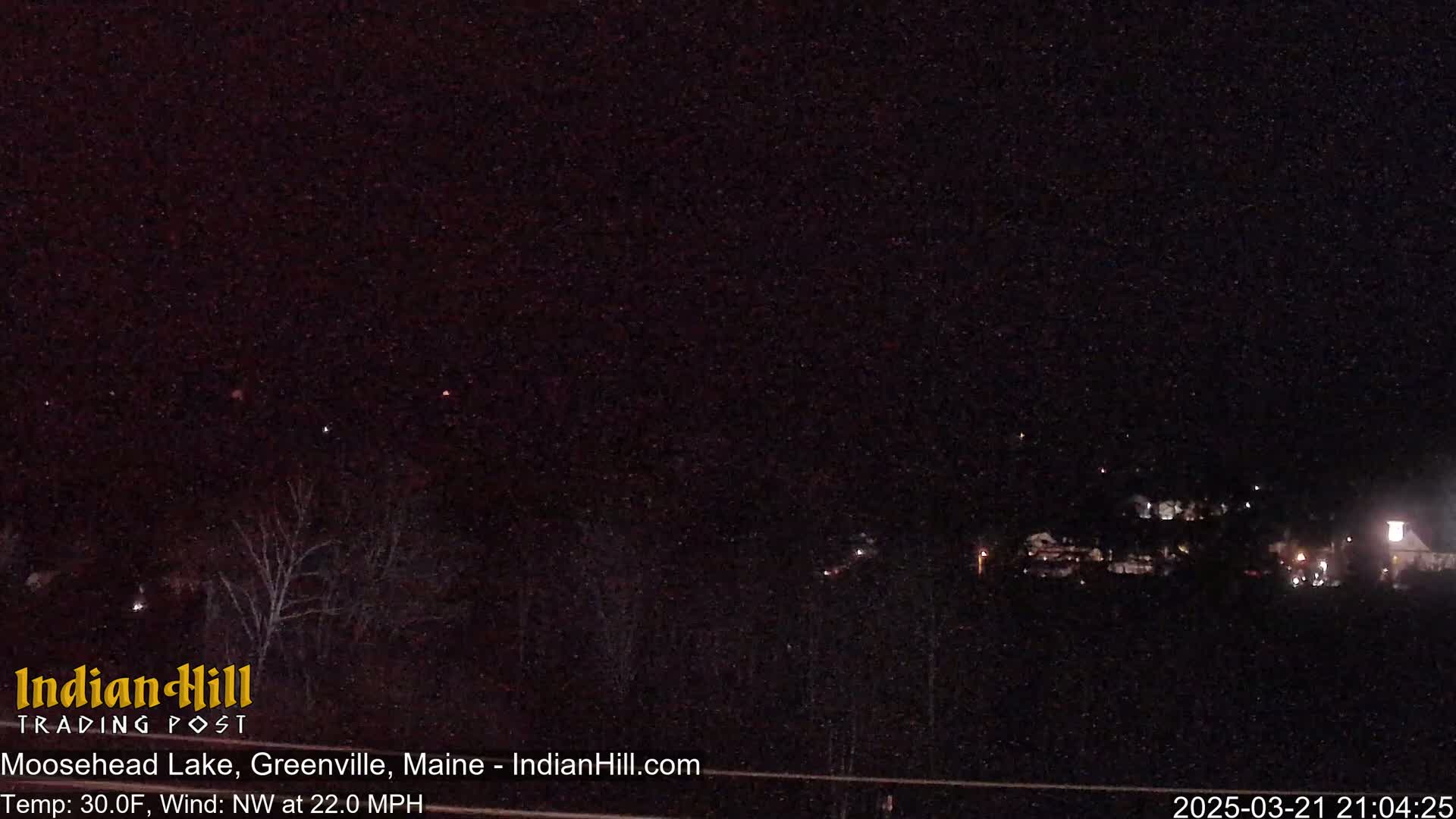 A nighttime view of a snow-covered landscape under a dark sky with a strong northwest wind.