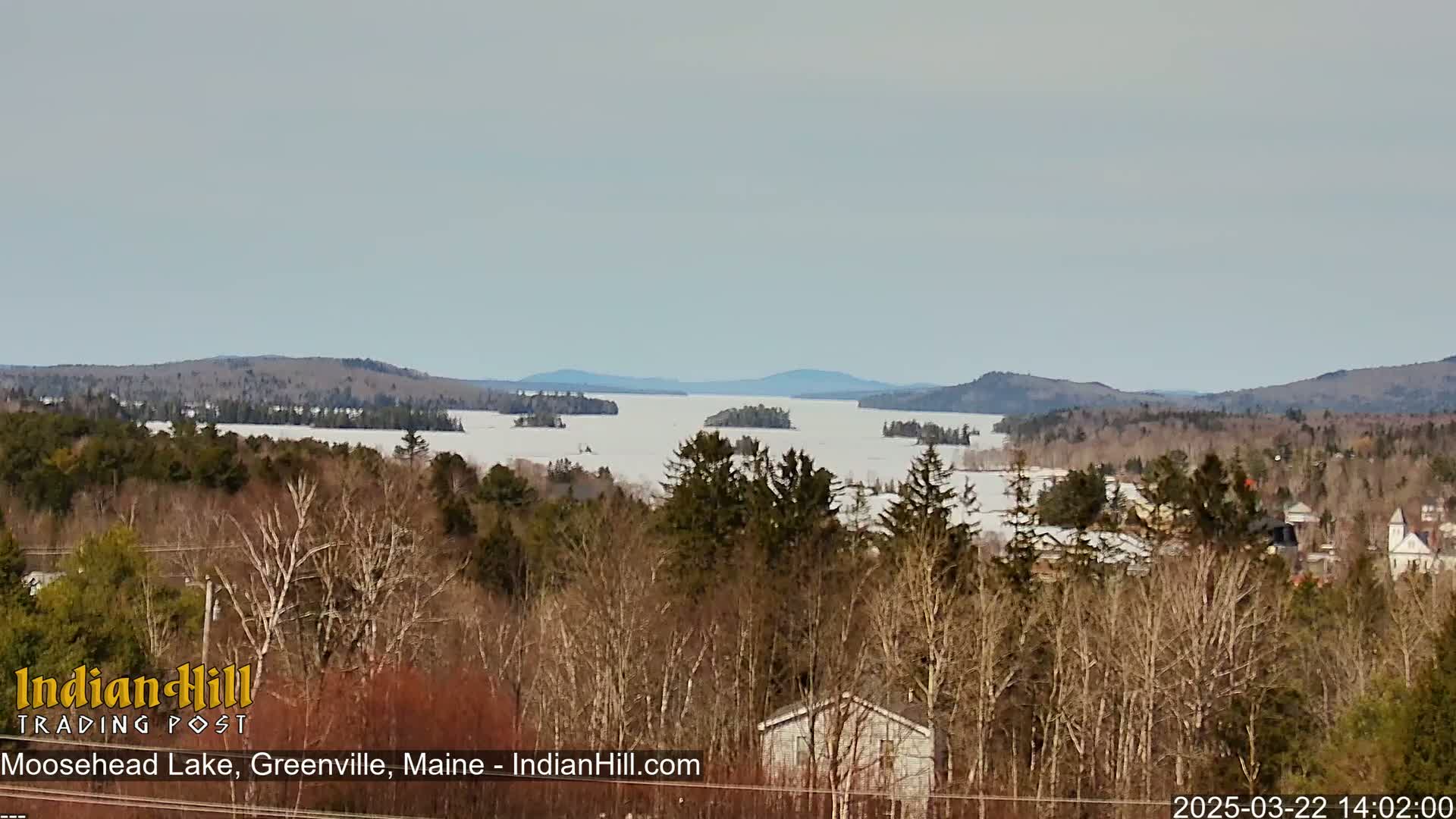 A partially frozen lake is seen from a forested hillside under a mostly clear sky.