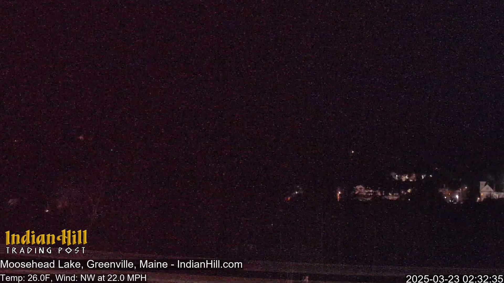 A nighttime view of dimly lit buildings in the distance under a dark sky with a northwest wind at 22 mph and a temperature of 26°F.