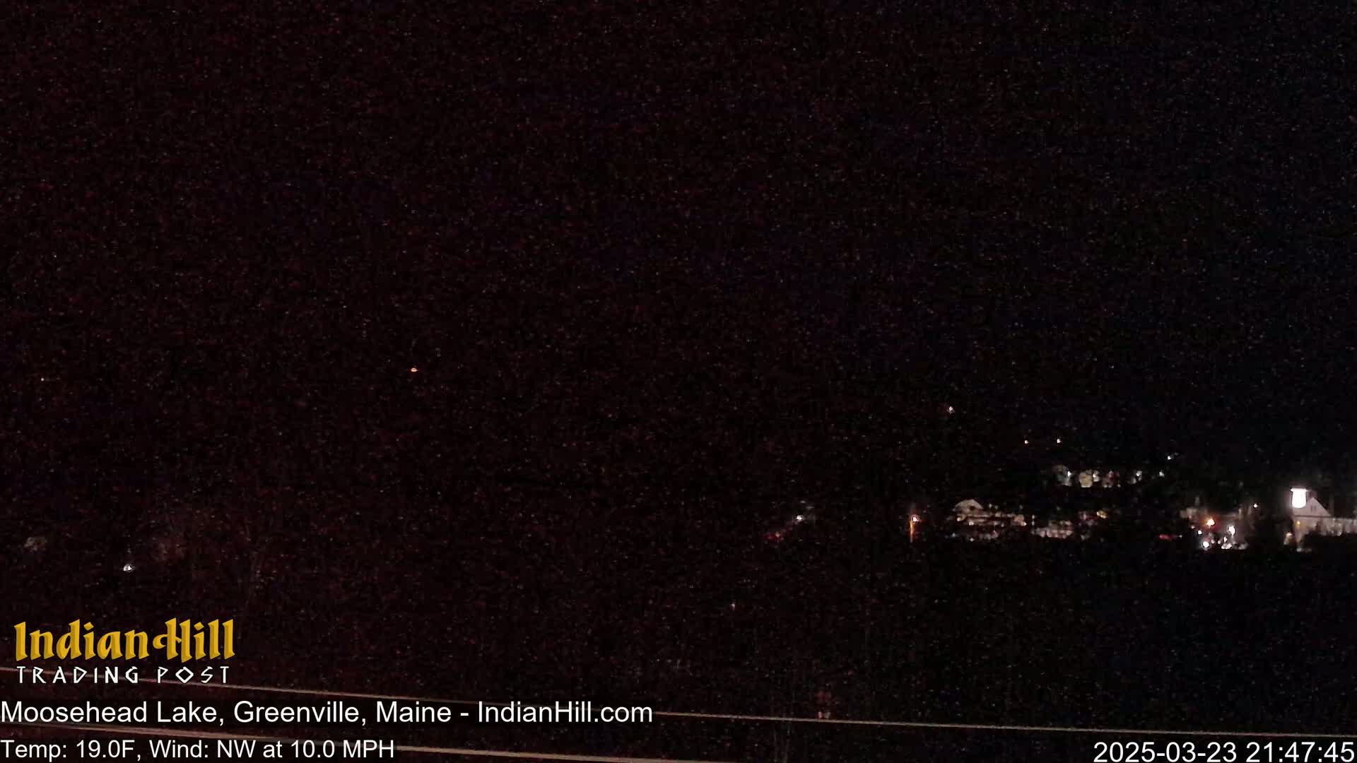 A nighttime, long shot of a town with a few lights visible under a dark, clear sky, with a northwest wind blowing at 10 mph and a temperature of 19 degrees Fahrenheit.
