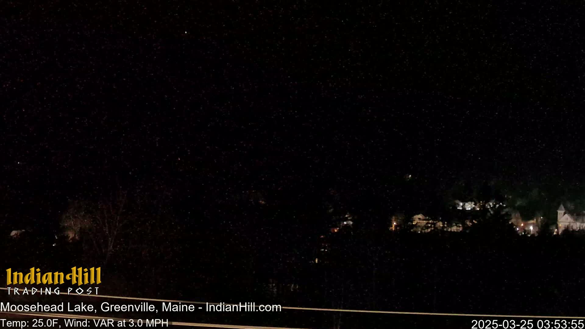 A nighttime view of a dark, starry sky over a line of dimly lit buildings and trees under a clear, cold sky.
