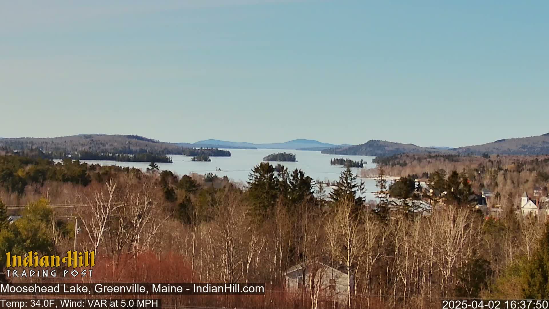 A partly frozen lake stretches to distant hills under a clear sky.