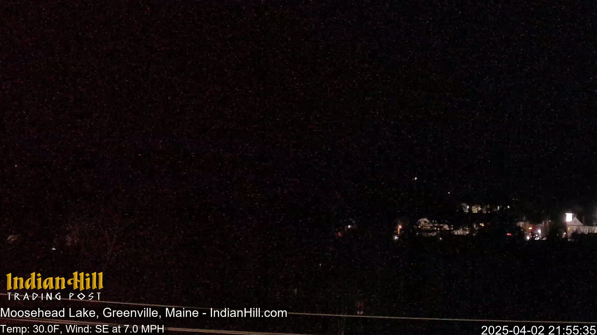 A nighttime view of dimly lit buildings and trees under a dark, starry sky with a southeast wind blowing at 7 mph and a temperature of 30 degrees Fahrenheit.