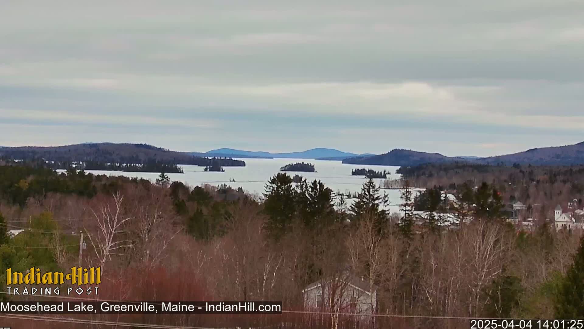 A partially frozen lake with numerous islands is seen from a high vantage point under an overcast sky.