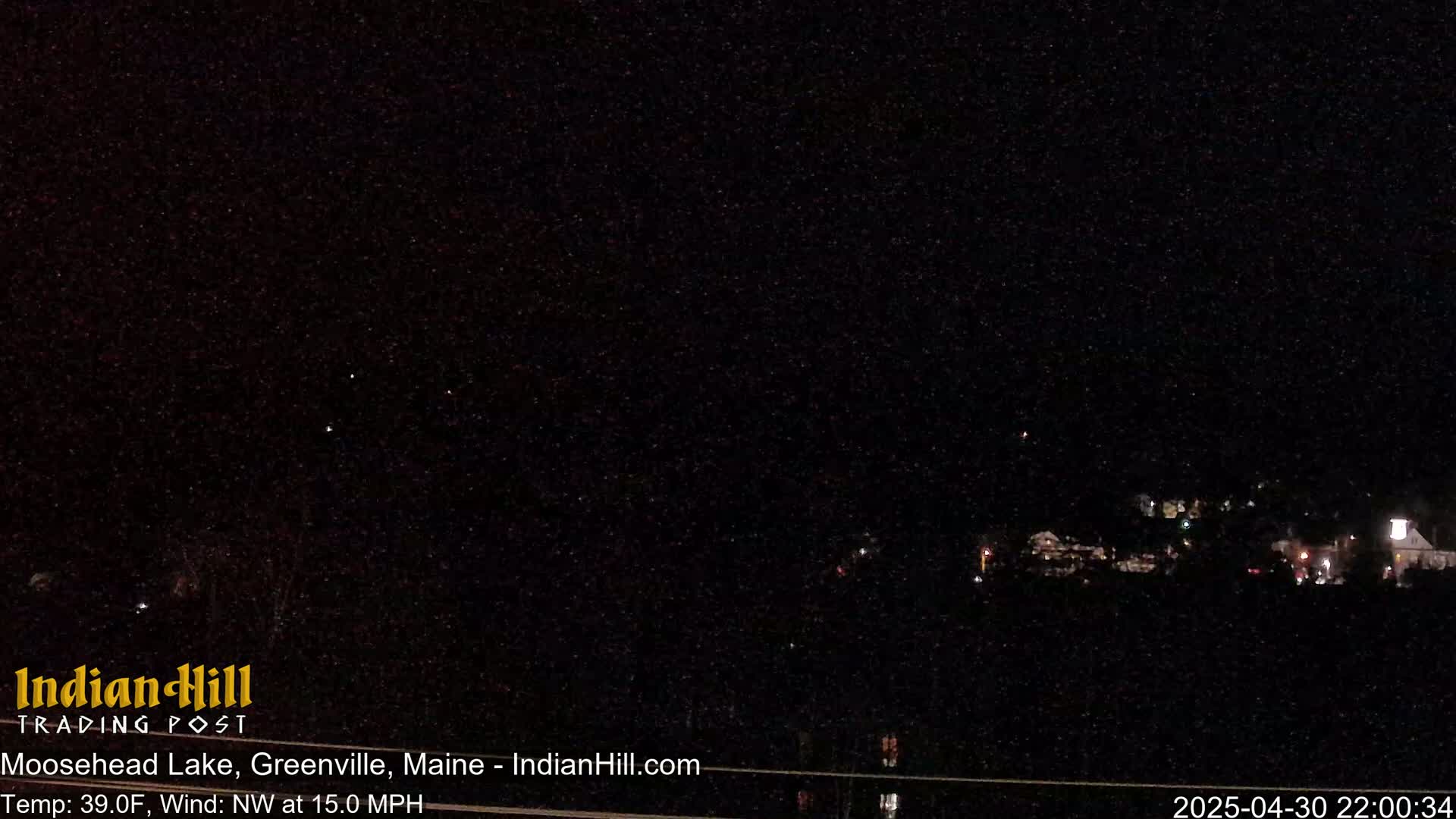 A nighttime long shot of a dimly lit town under a dark, clear sky with a northwest wind of 15 mph and a temperature of 39°F.