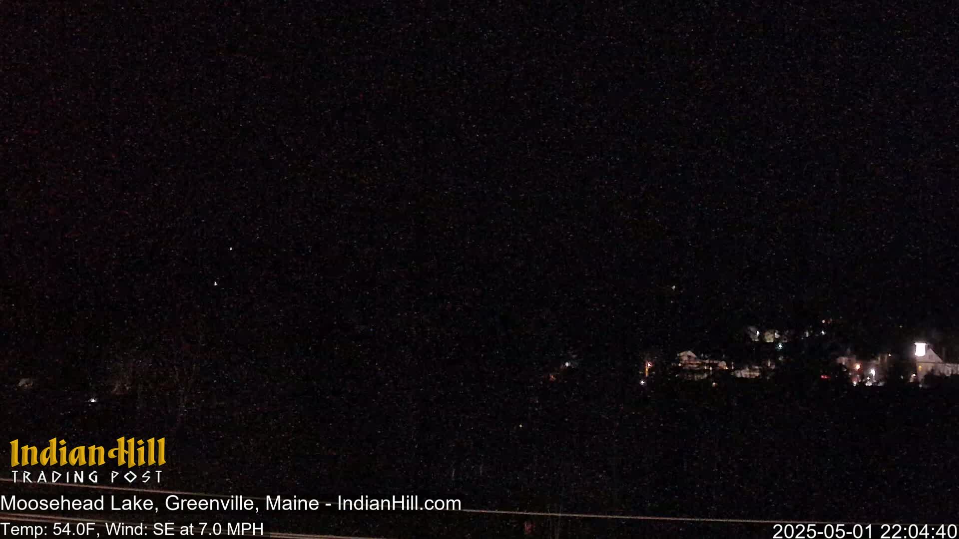A nighttime long shot shows a dark landscape with a few faint lights in the distance under a clear, dark sky.