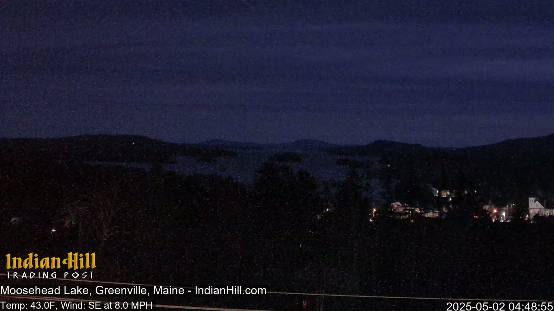 A nighttime view of a lake and distant town under snowy conditions, with a dark sky.