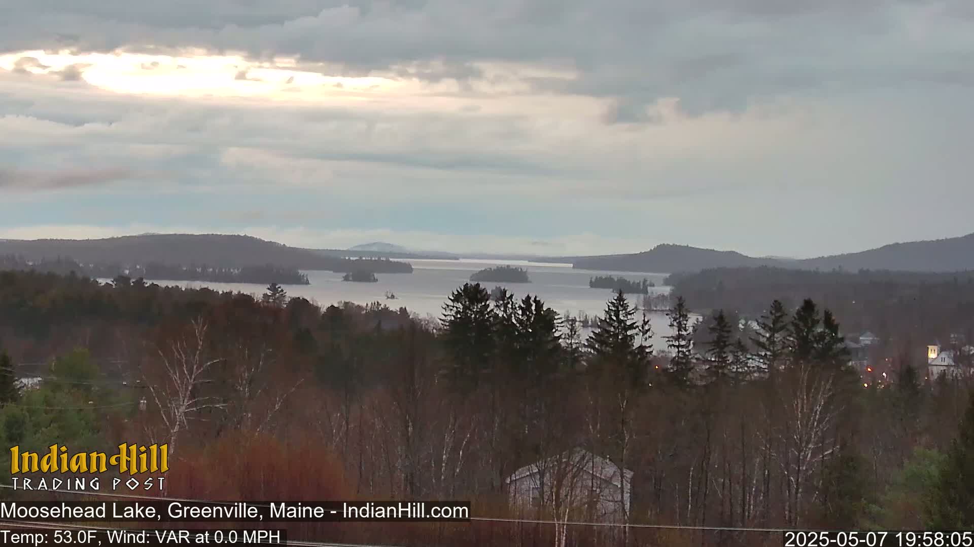 A mostly cloudy, cool day overlooks a large lake dotted with islands and surrounded by dark green forests.