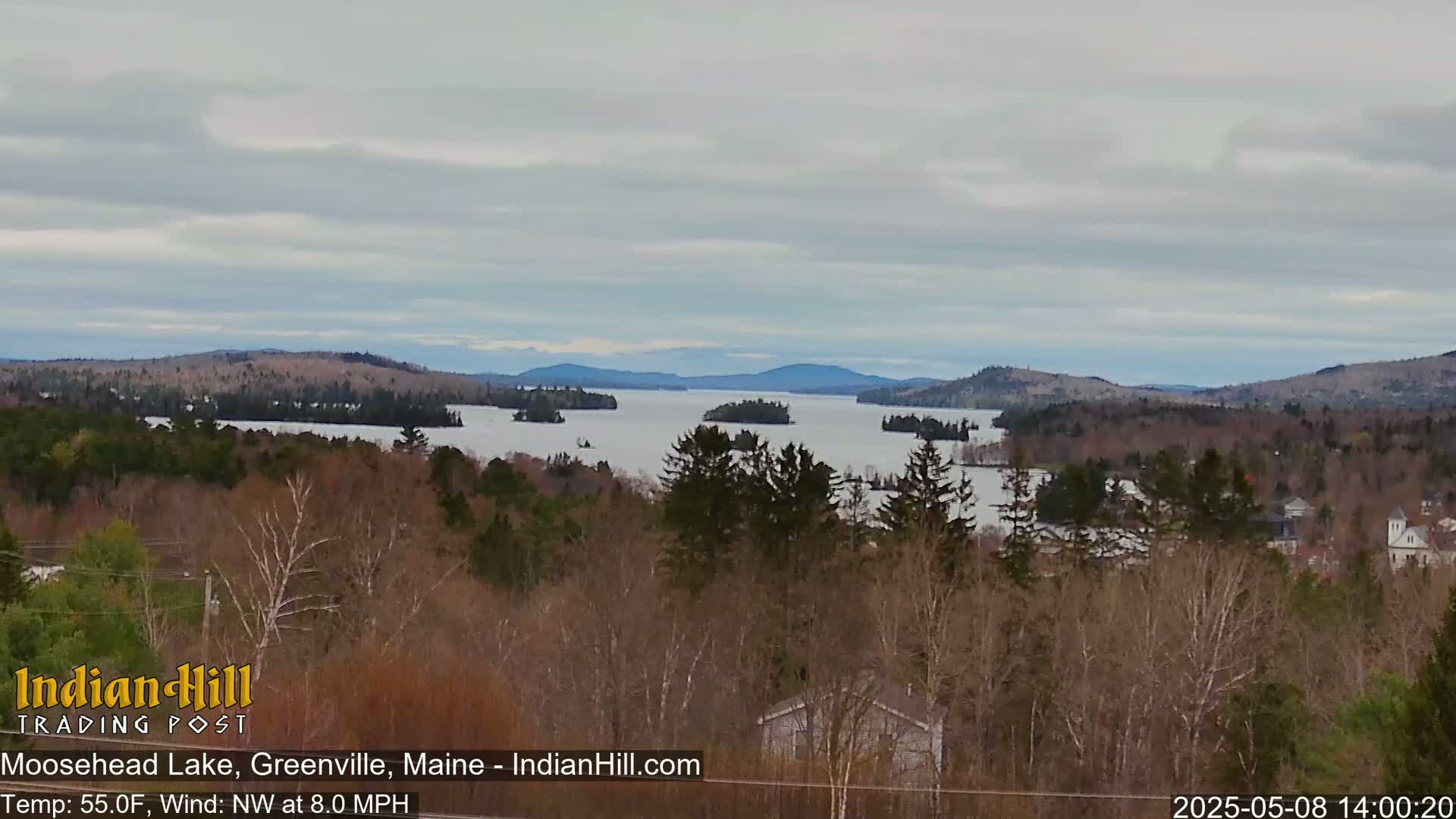 A view of a large lake with many islands, surrounded by trees and mountains under a cloudy sky.