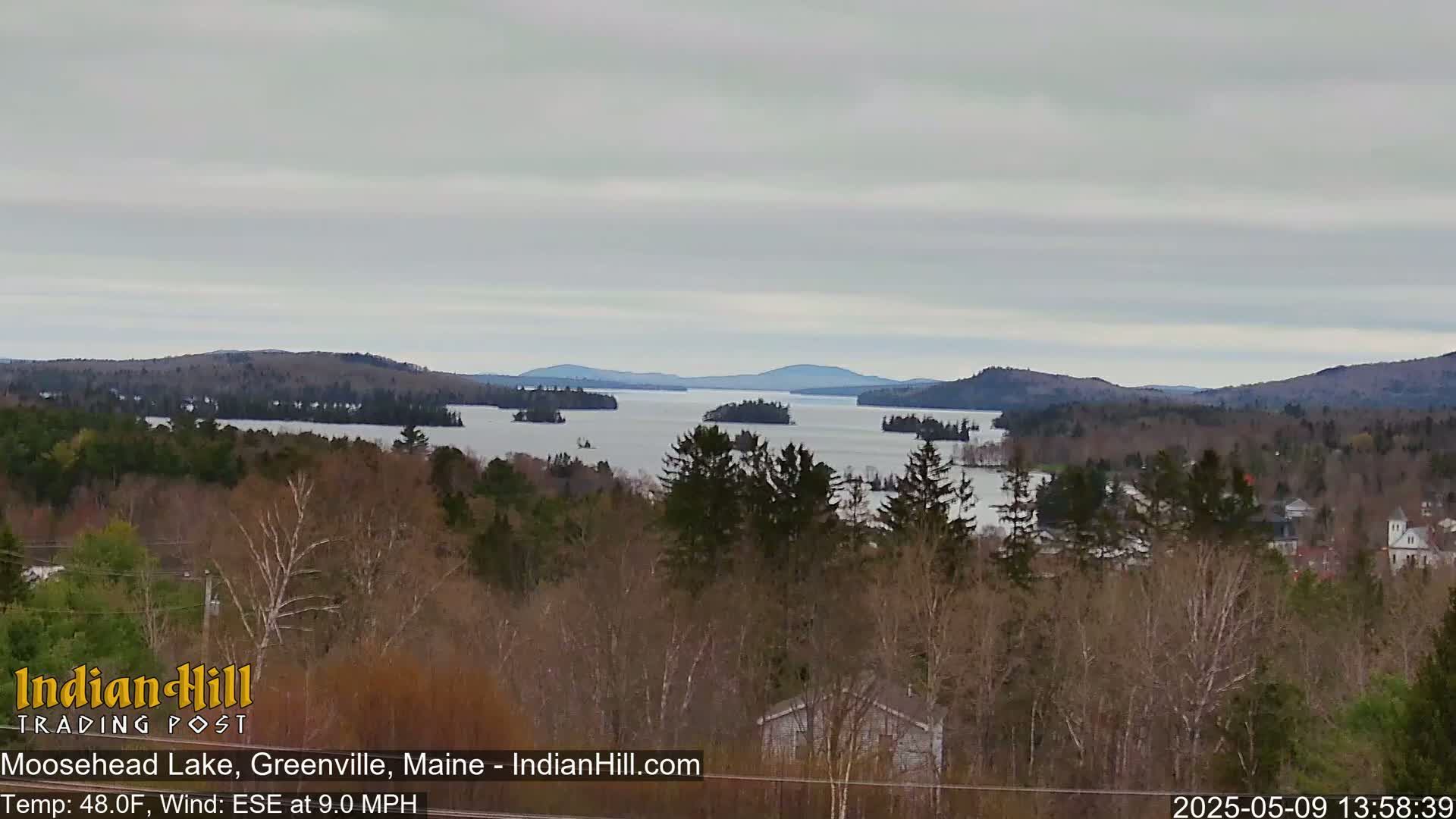 A wide, expansive view of a lake dotted with islands, surrounded by a forest under an overcast sky.
