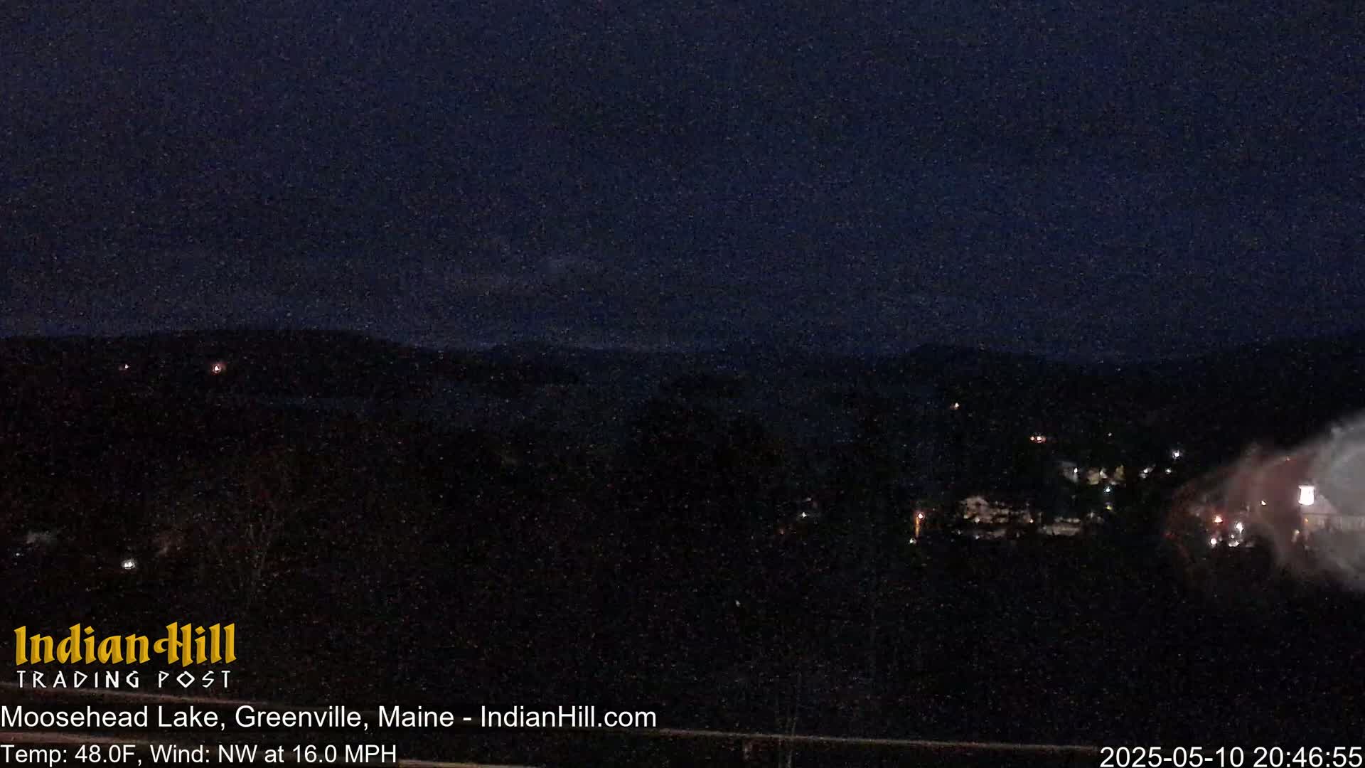 A nighttime, long shot of a dark landscape with scattered lights, under a dark, possibly cloudy sky, with a northwest wind of 16 mph.