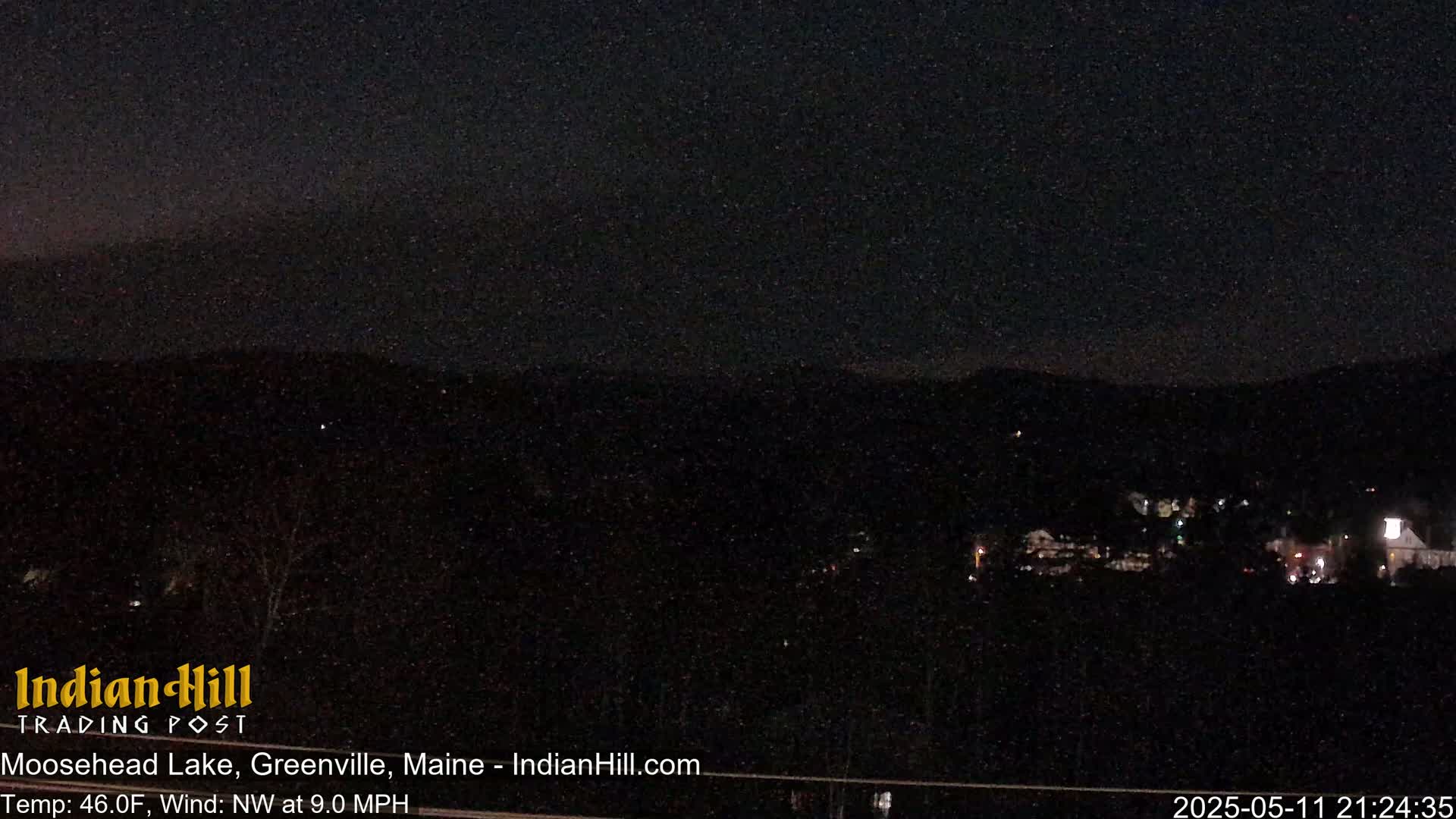 A nighttime view of a dark landscape with a few distant lights under a starry sky.