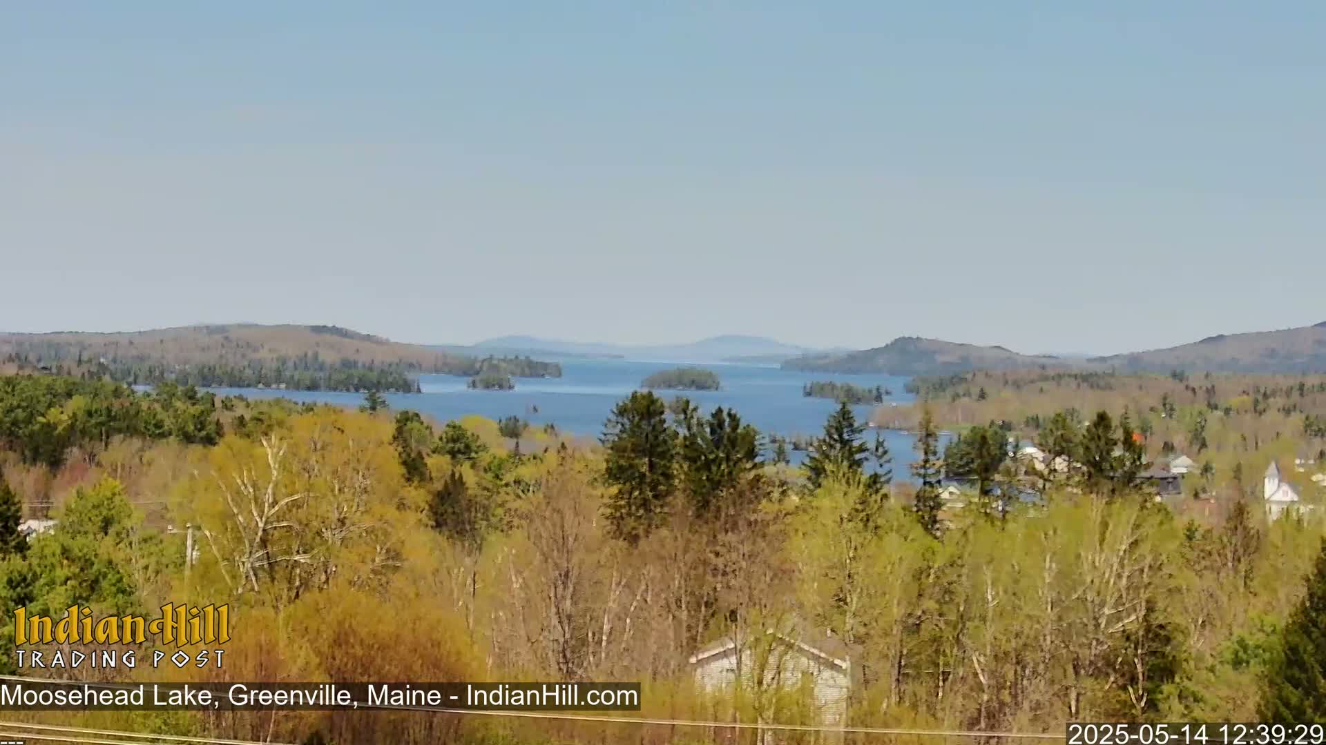 A vast lake dotted with islands stretches to tree-covered hills under a clear, light blue sky.