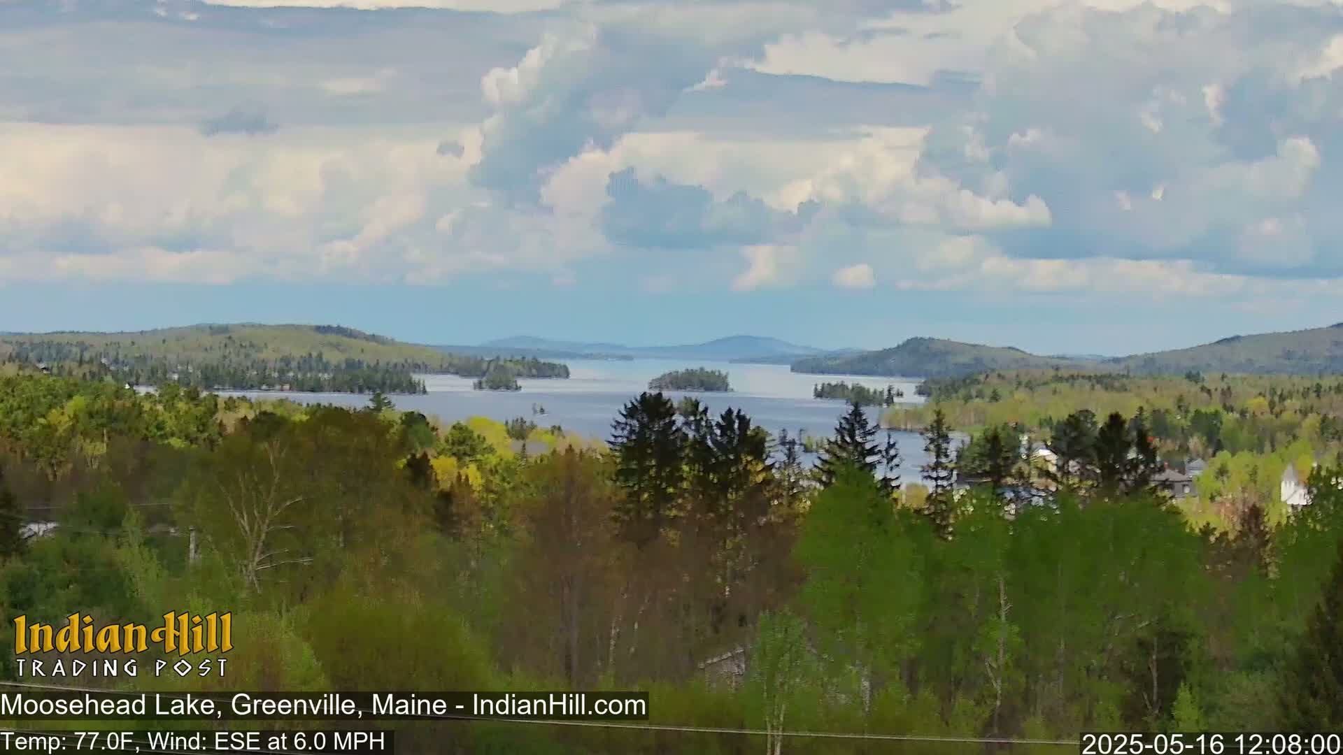 A partly cloudy day shows a view of a lake with islands and forested hills under a partly cloudy sky.
