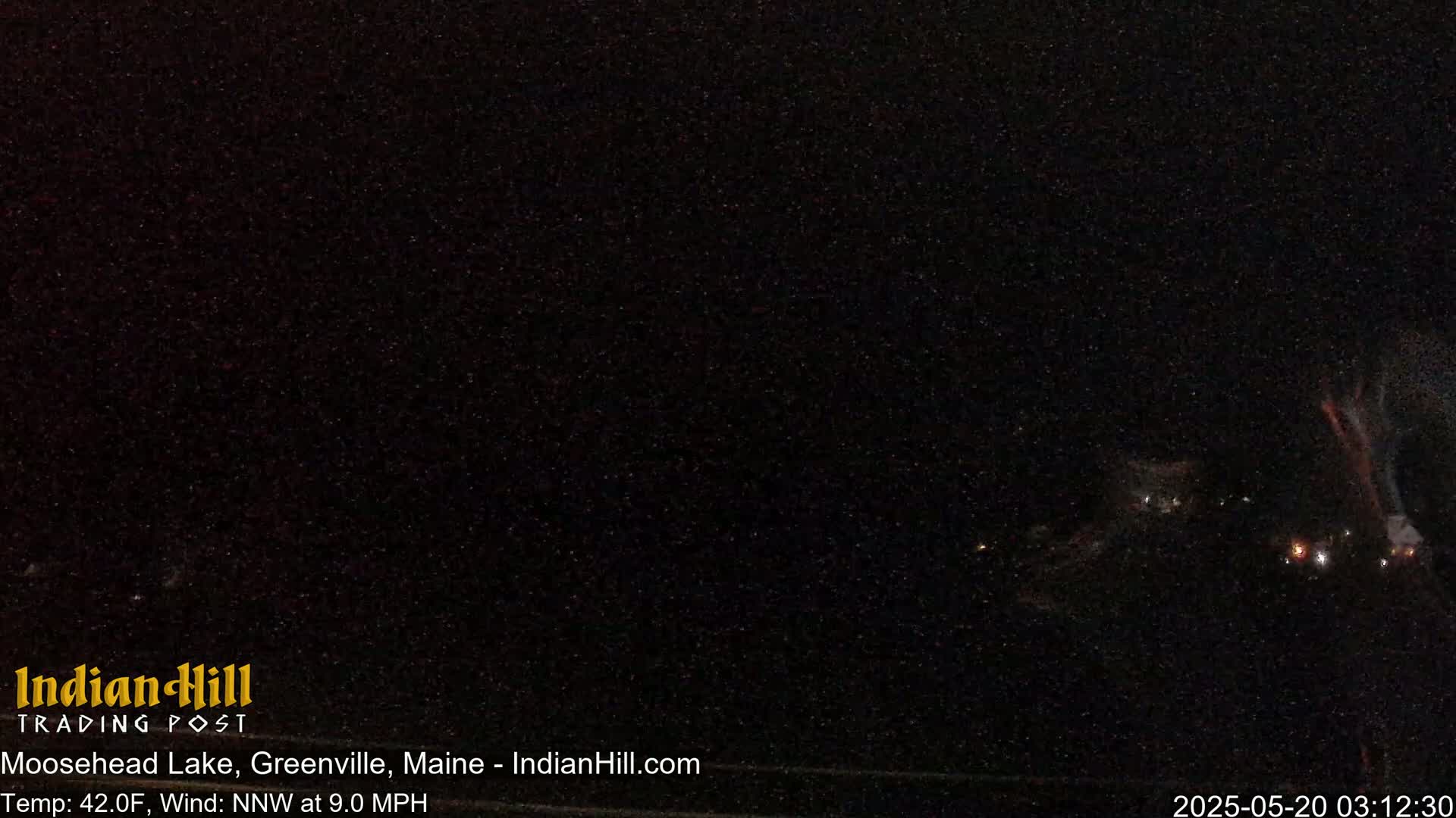 A nighttime, long shot of a dark landscape with a few distant, faint lights and a north-northwest wind at 9.0 mph and a temperature of 42°F.