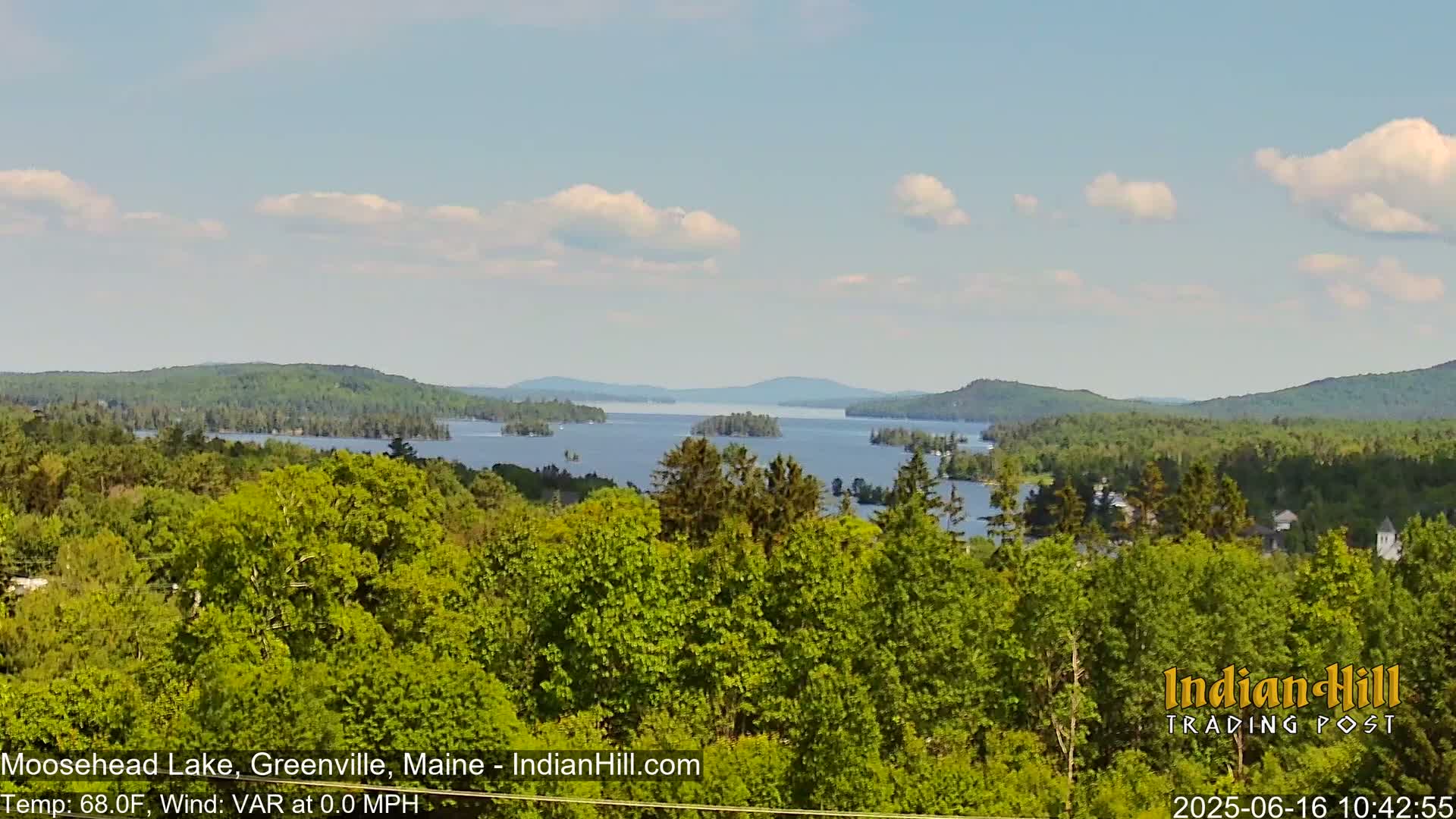 A panoramic view of a lake dotted with islands and surrounded by lush green forests under a partly cloudy sky.