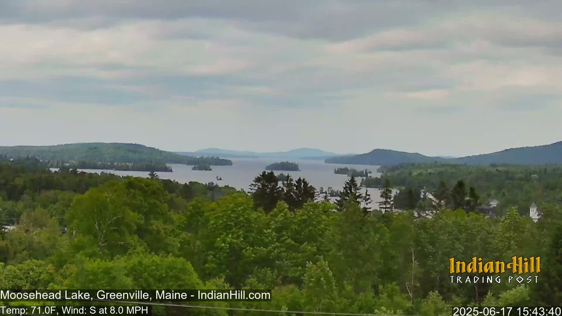 A view of a lake with many islands and forested hills under a partly cloudy sky.
