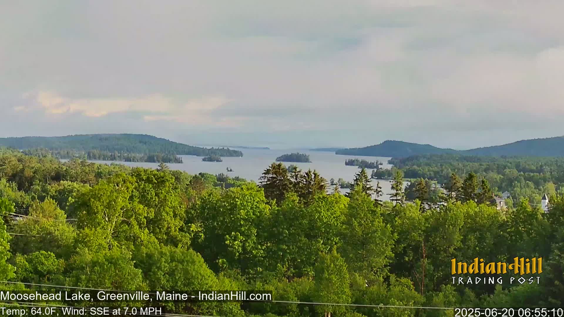 A tranquil view of a lake dotted with islands, surrounded by lush green forests under a partly cloudy sky.