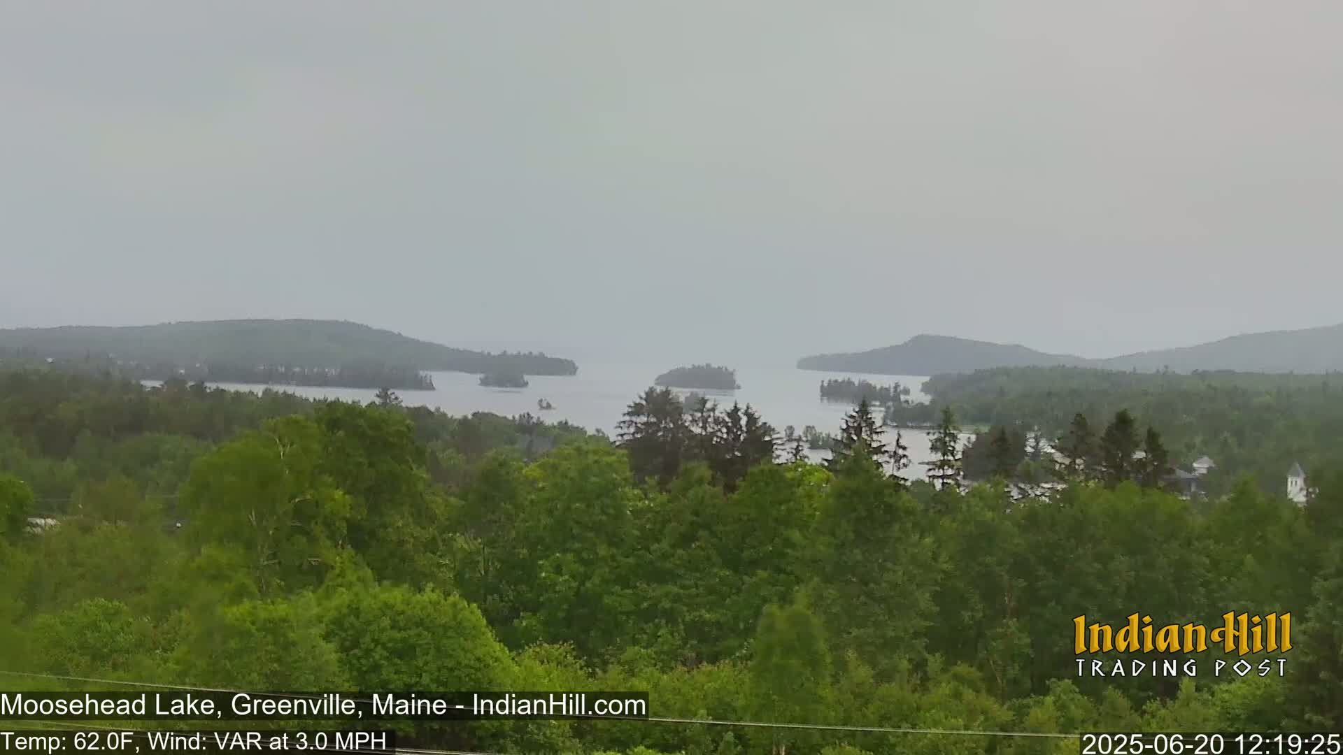 A hazy view shows a lake with islands surrounded by lush green trees under an overcast sky.