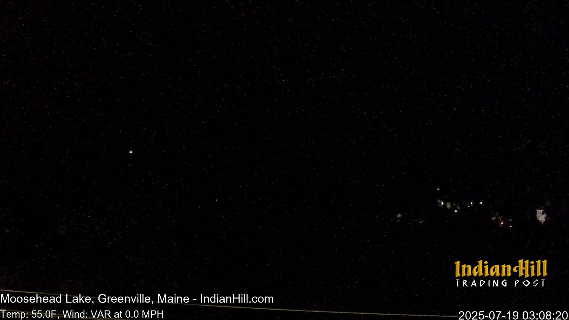 A nighttime, dark outdoor scene shows a few distant lights on the horizon under a clear, star-filled sky.