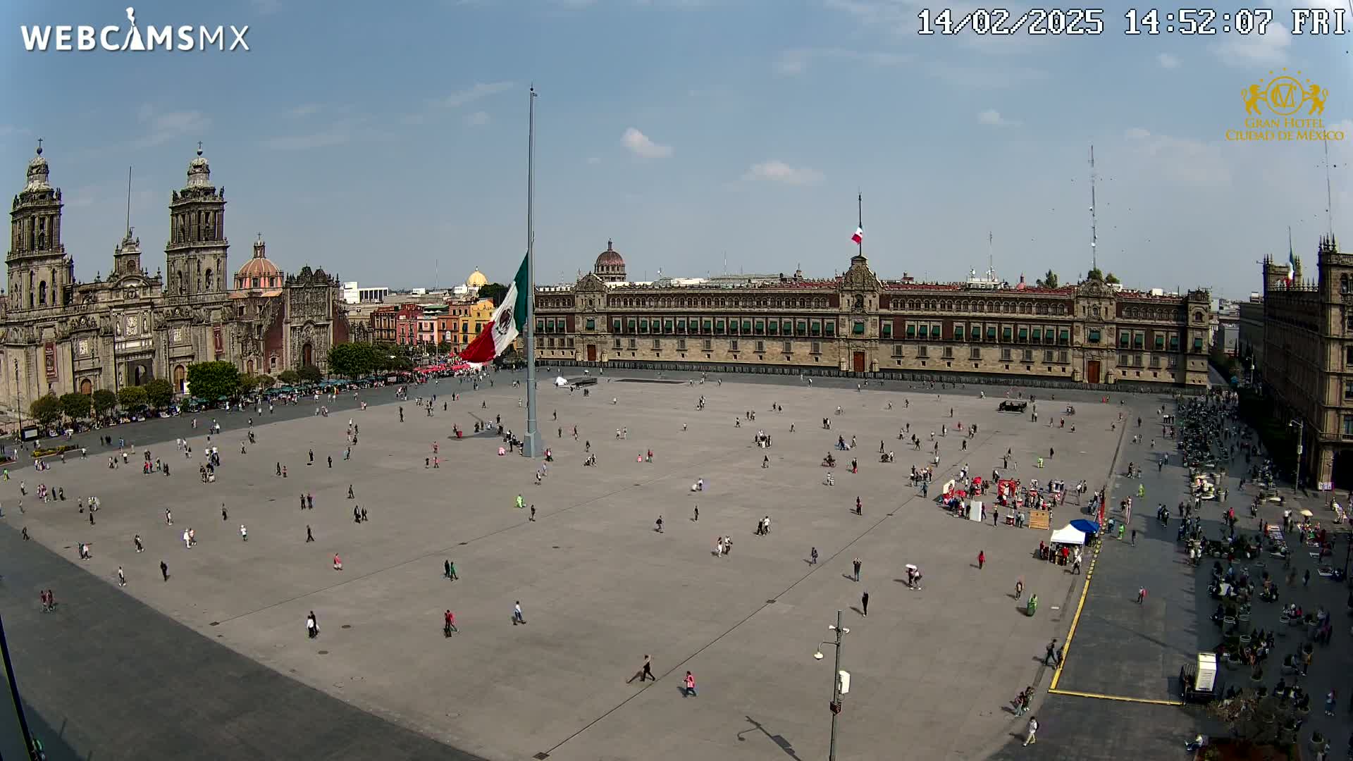 A large plaza with sparse crowds is surrounded by historical buildings under a mostly sunny sky.