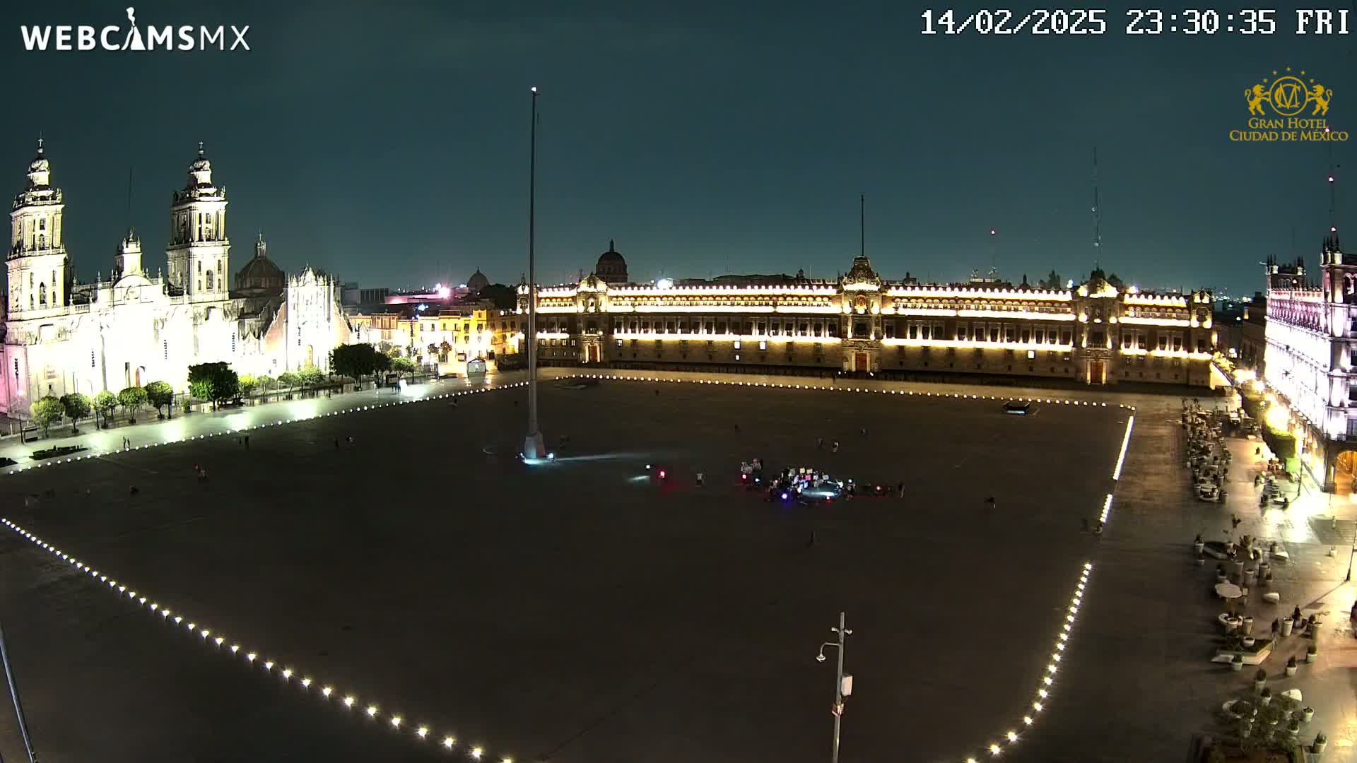 A large, mostly empty plaza at night is illuminated, showing a cathedral and government buildings.