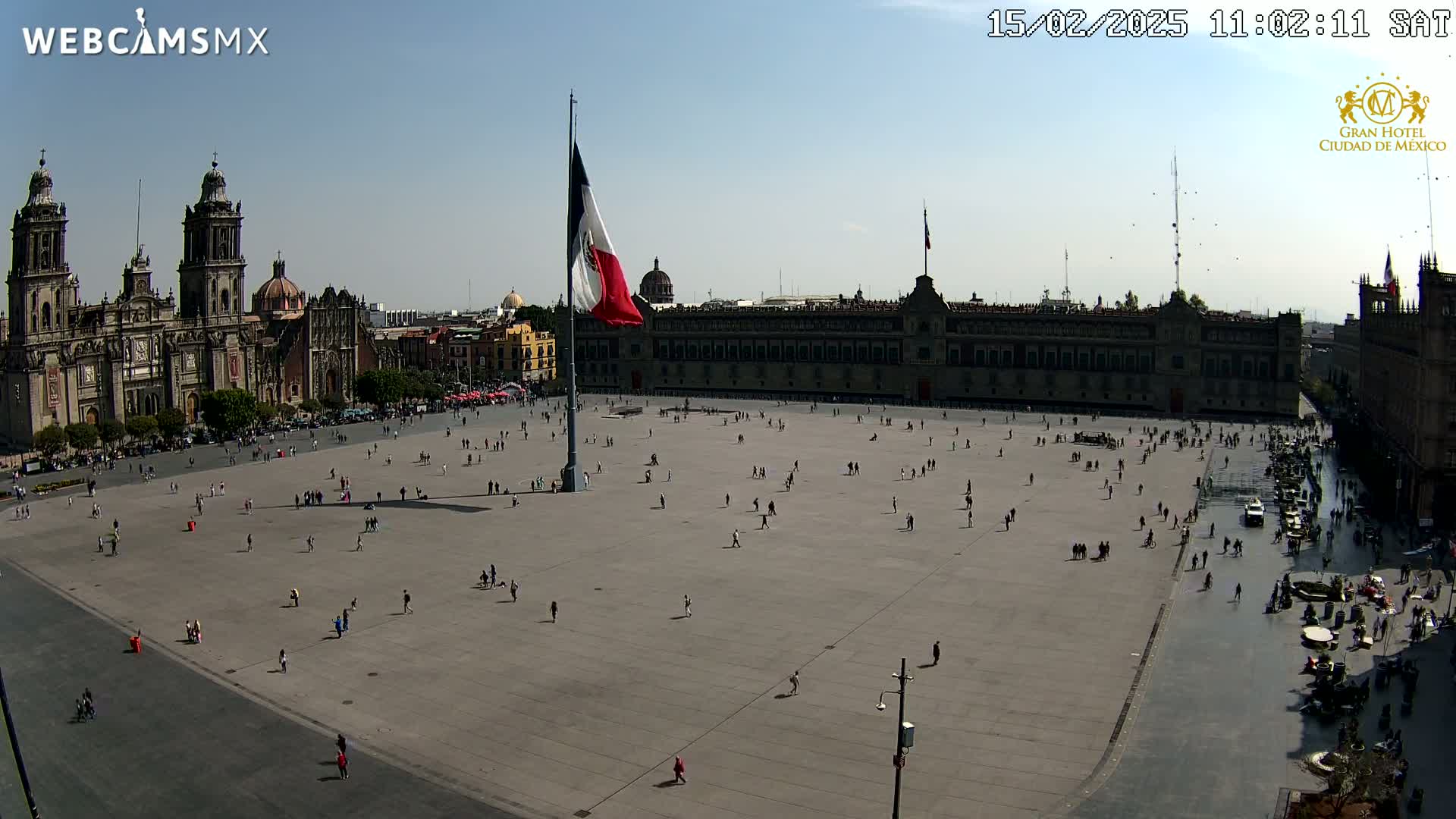 A large plaza with a few people scattered across it, a large building and a cathedral in the background under sunny skies.