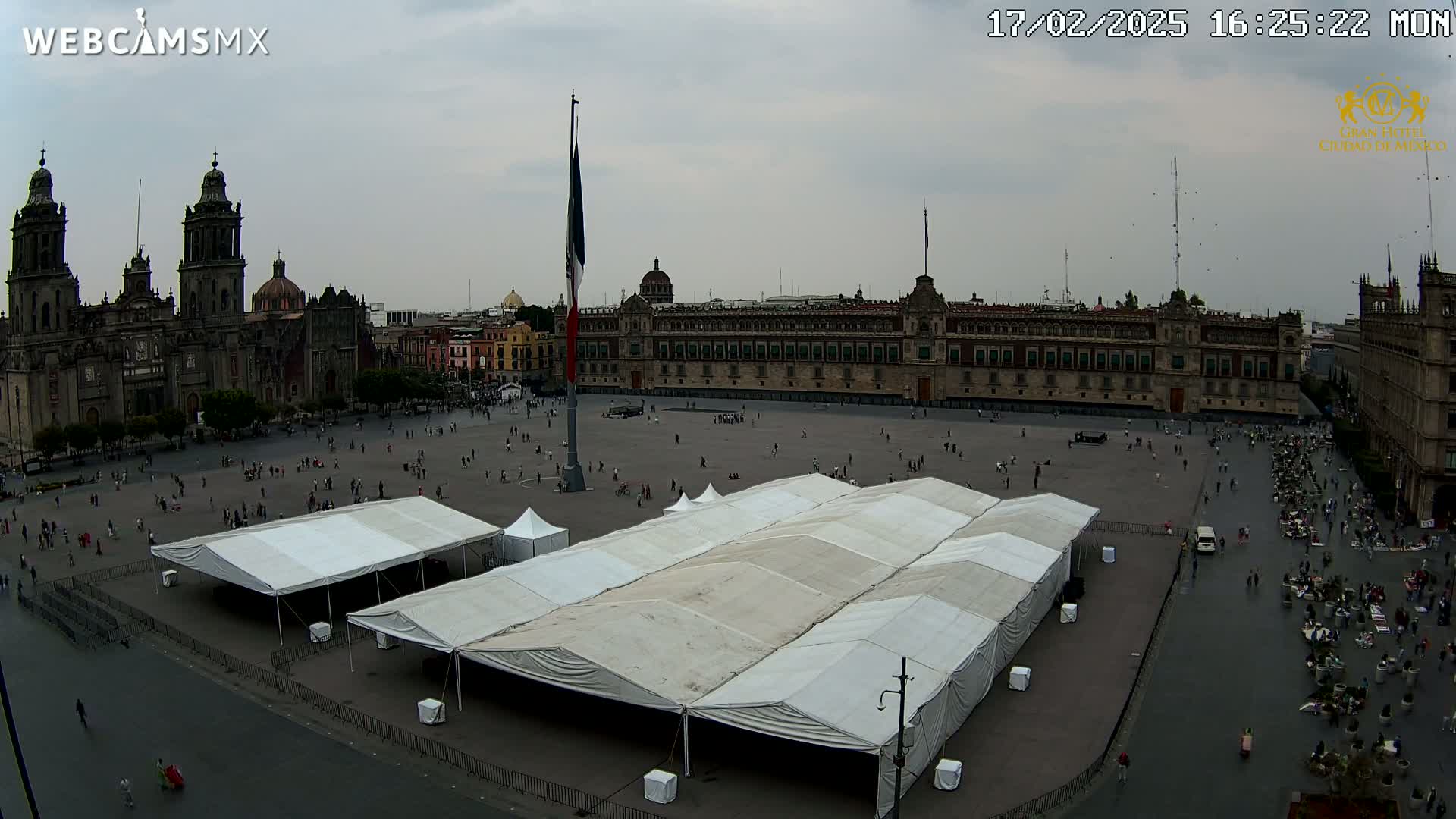 A large plaza with several white tents, a cathedral, and a long government building is seen under an overcast sky.