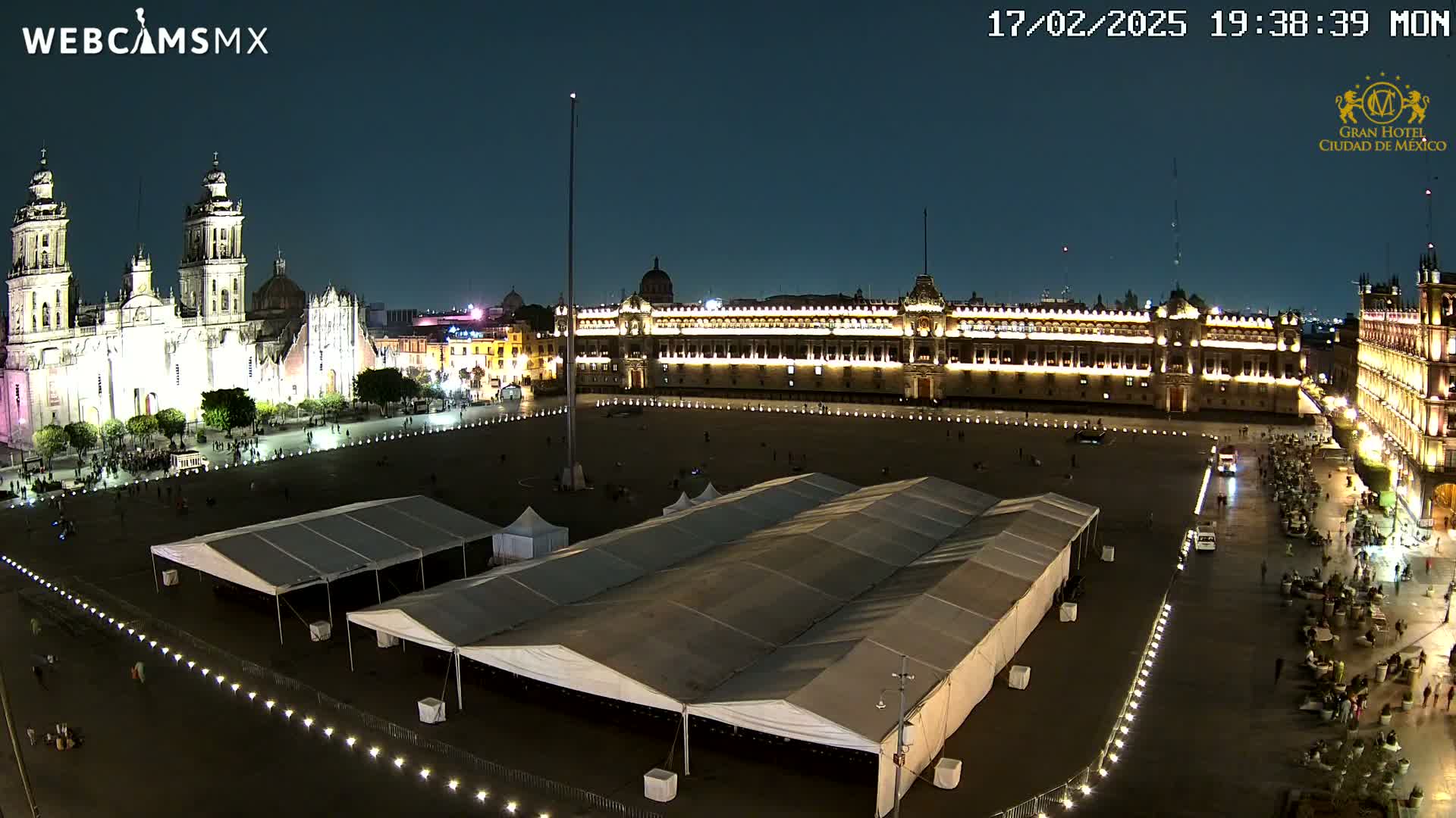 A nighttime, high-angle view of a large plaza with a cathedral and government buildings illuminated, featuring several large tents set up in the center.