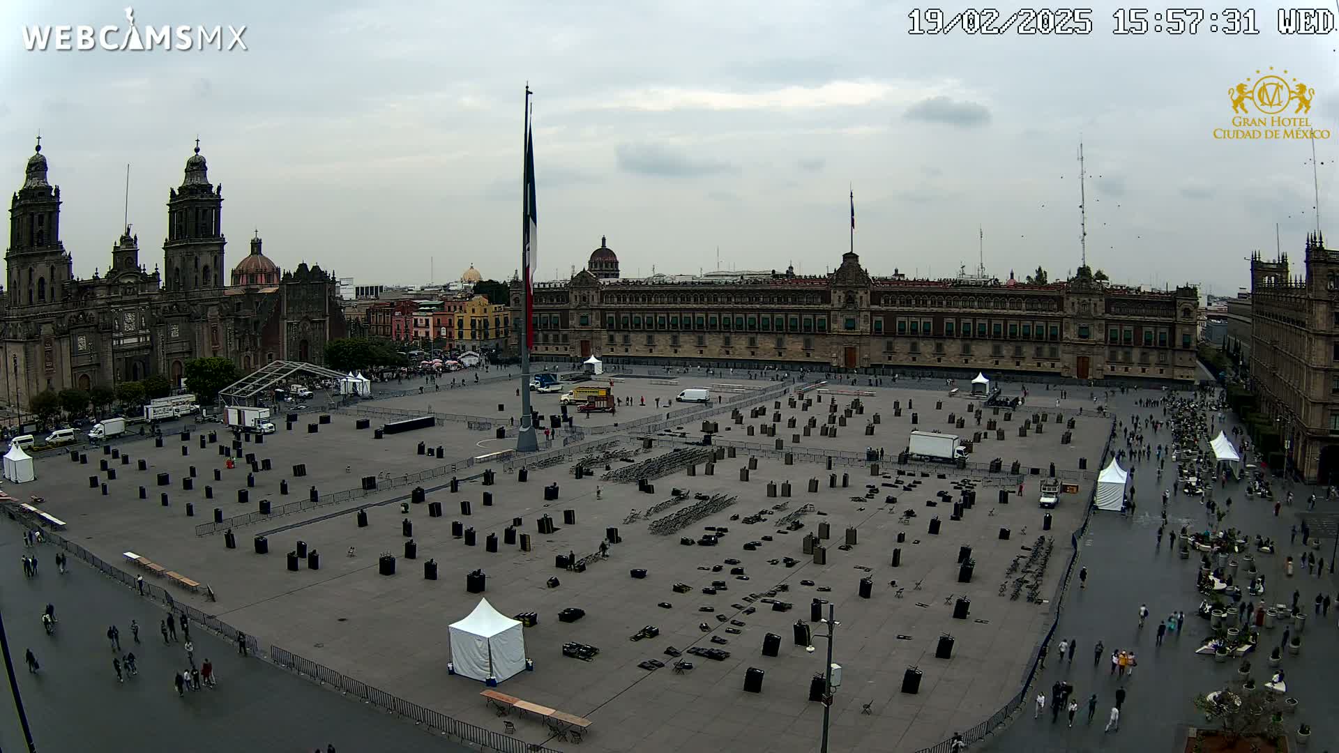 An overcast day reveals a large plaza with numerous black rectangular objects scattered across it, surrounded by historic buildings, including a cathedral and a long palace-like structure.
